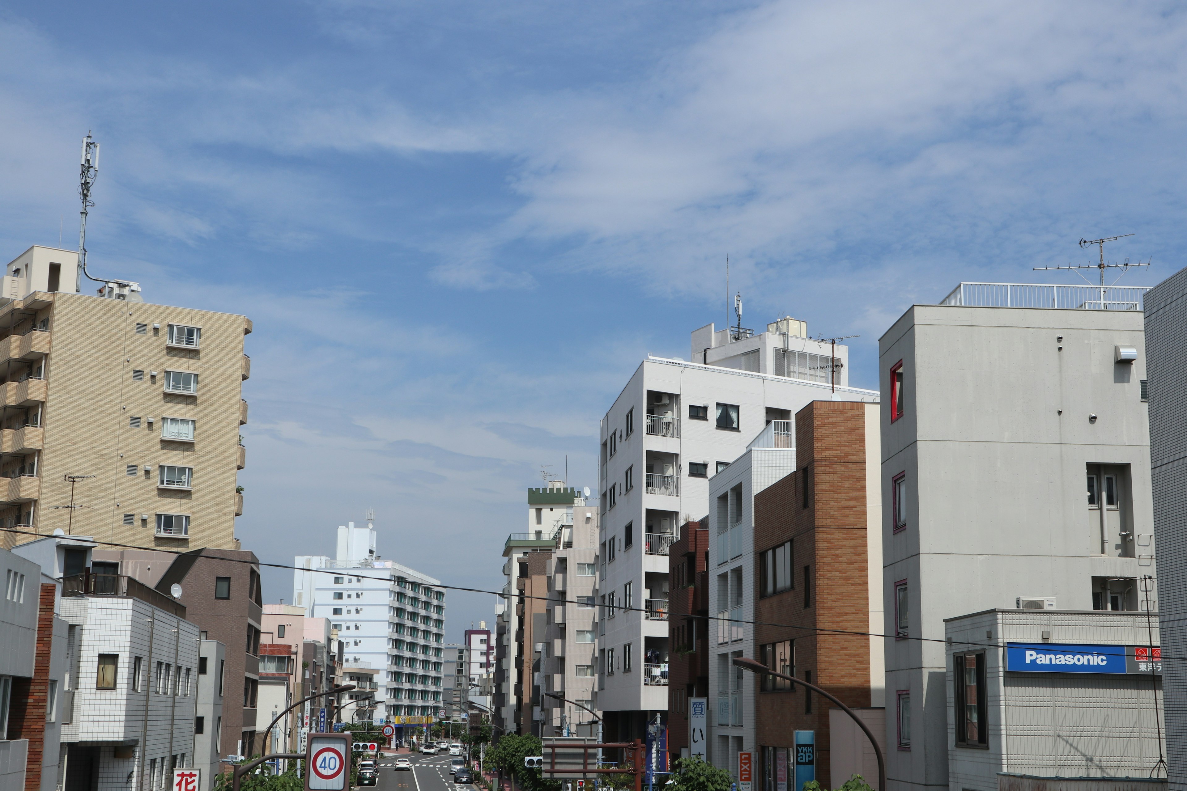 Paisaje urbano con cielo azul, edificios altos, calle, señales de tráfico, letrero de Panasonic