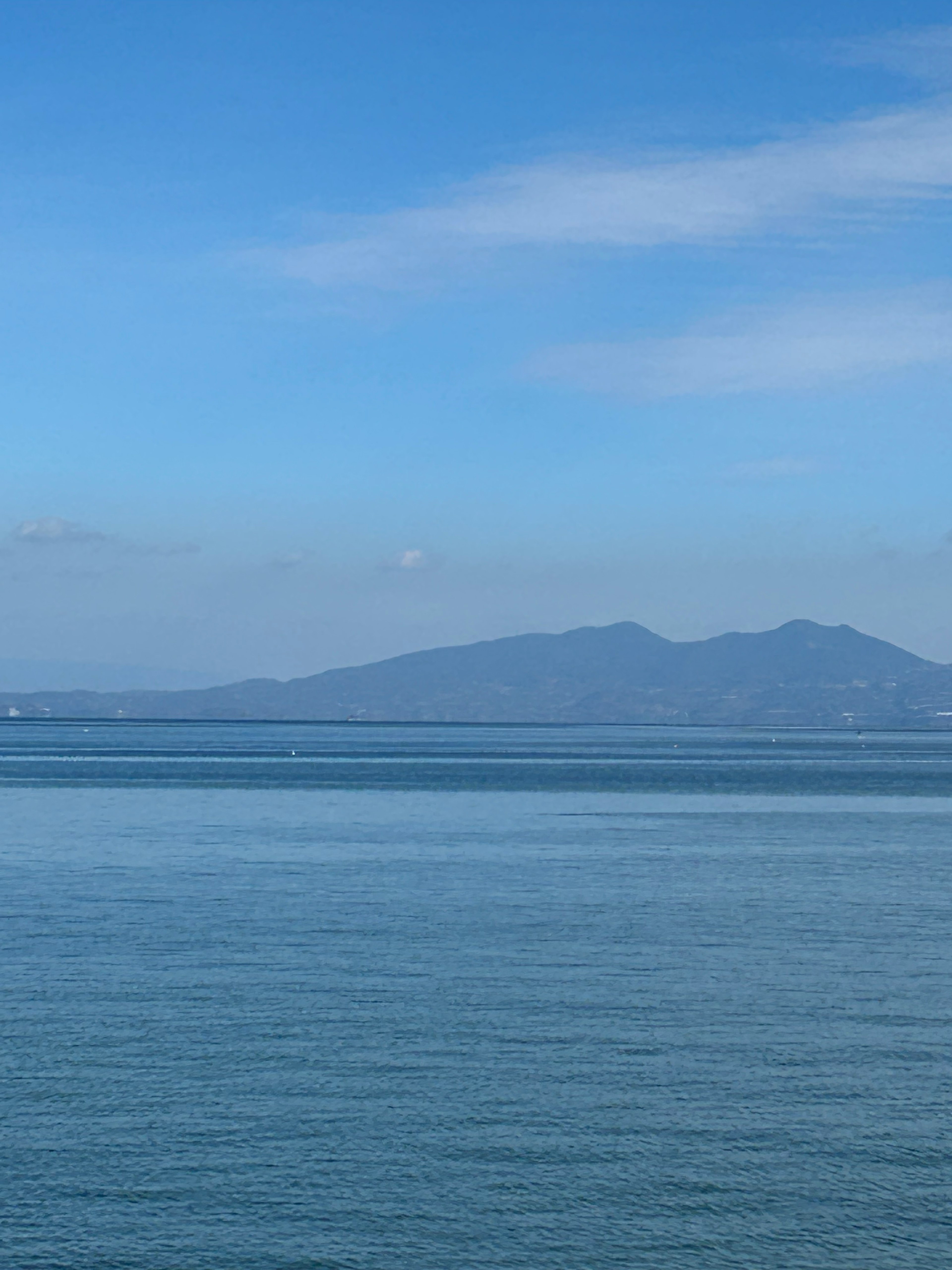 Pemandangan laut dan langit biru yang tenang dengan gunung di kejauhan