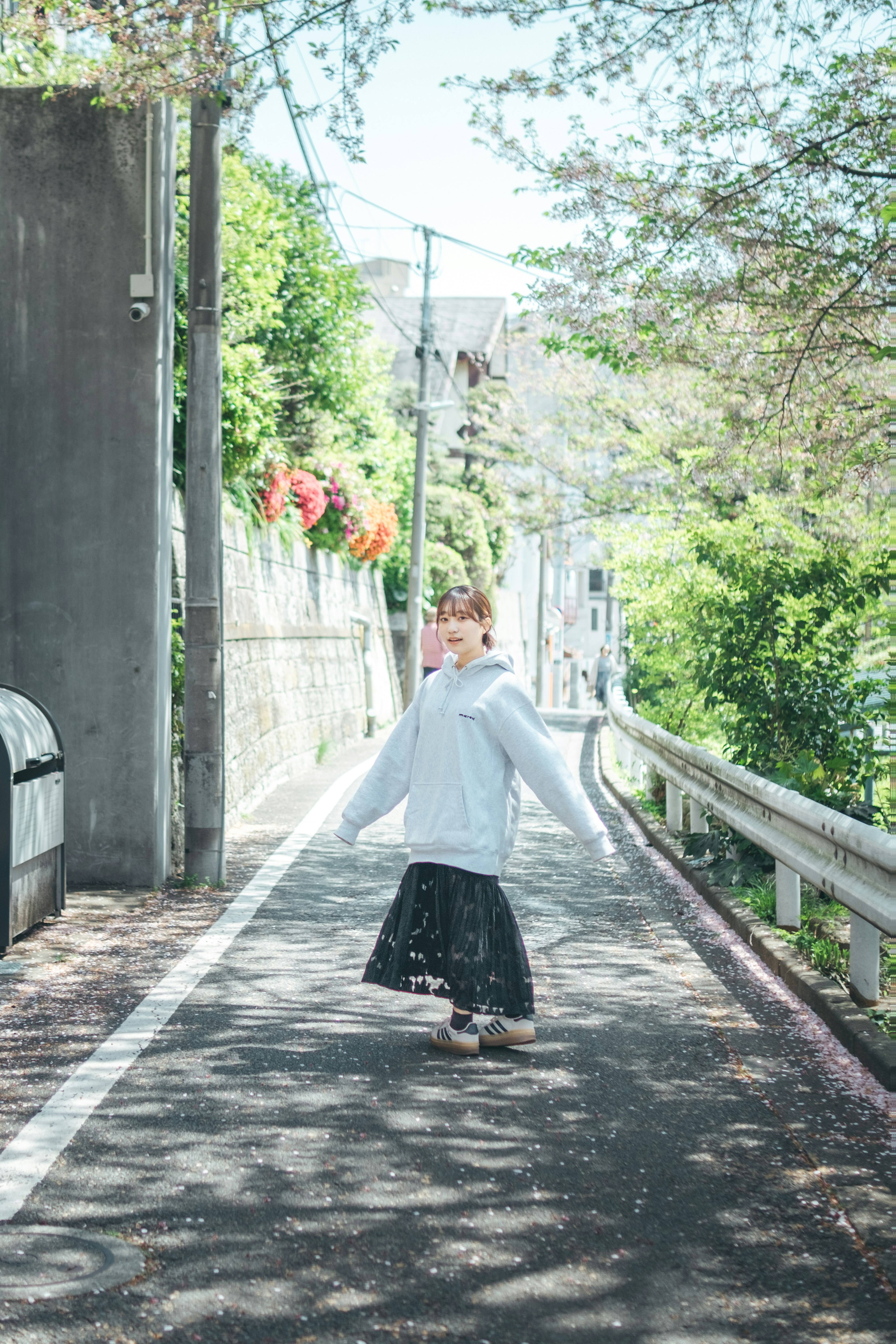 A woman in a white hoodie and black skirt walking down a quiet street from behind