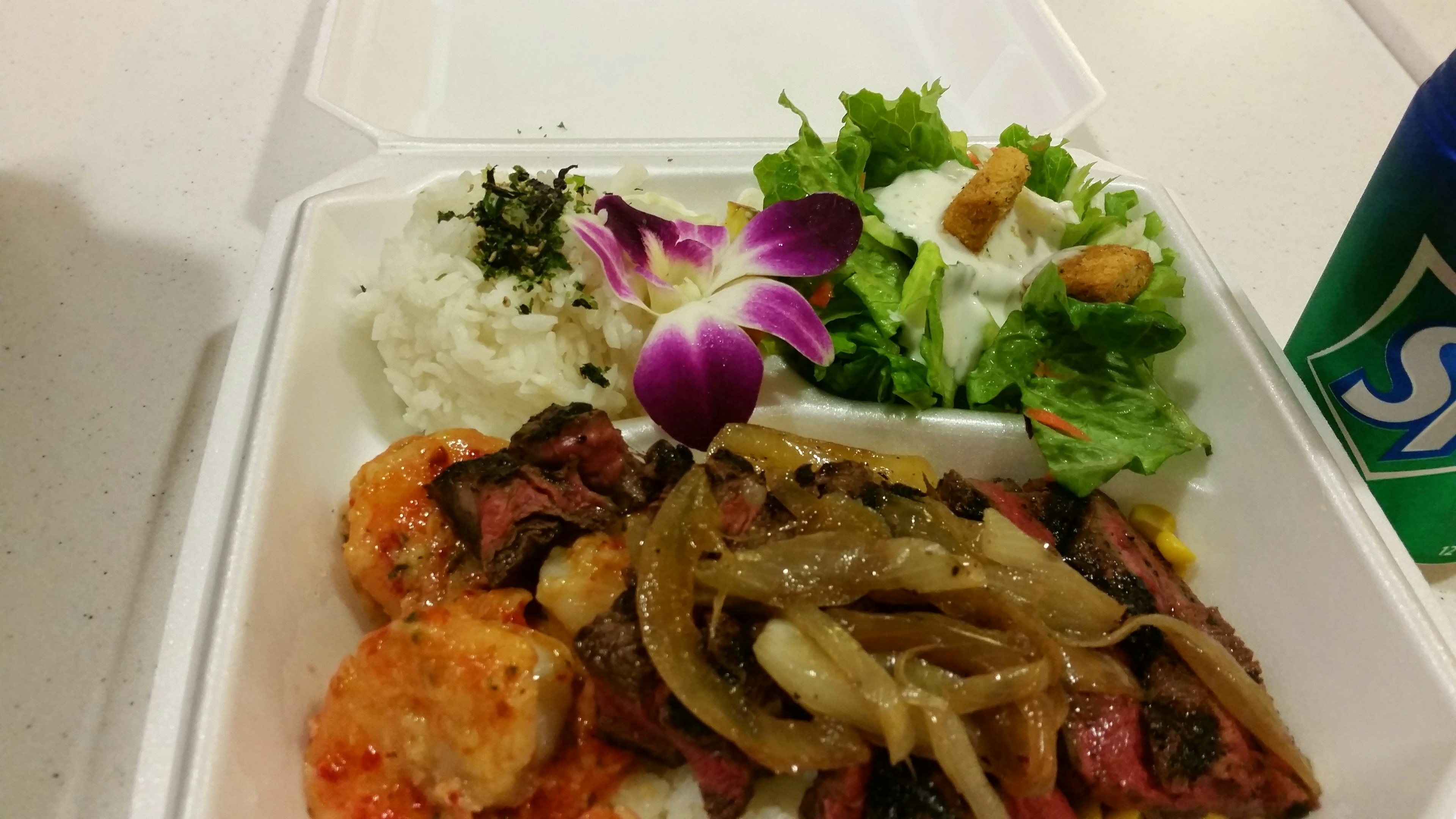 Comida deliciosa en un recipiente blanco con camarones, verduras, ensalada, arroz y adorno de flor morada