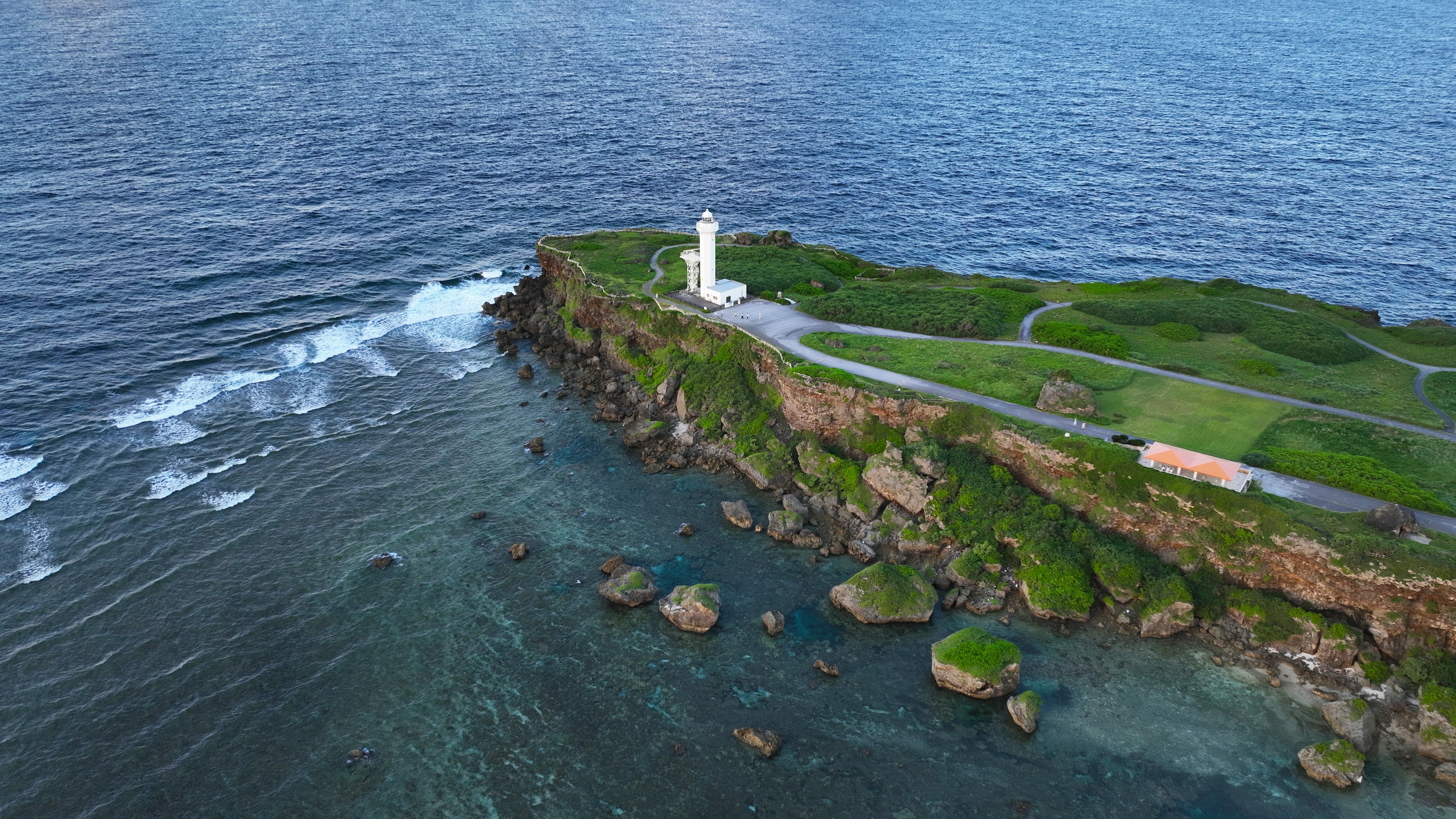 Malersicher Blick auf einen Leuchtturm auf einer grünen Klippe umgeben von Ozeanwellen