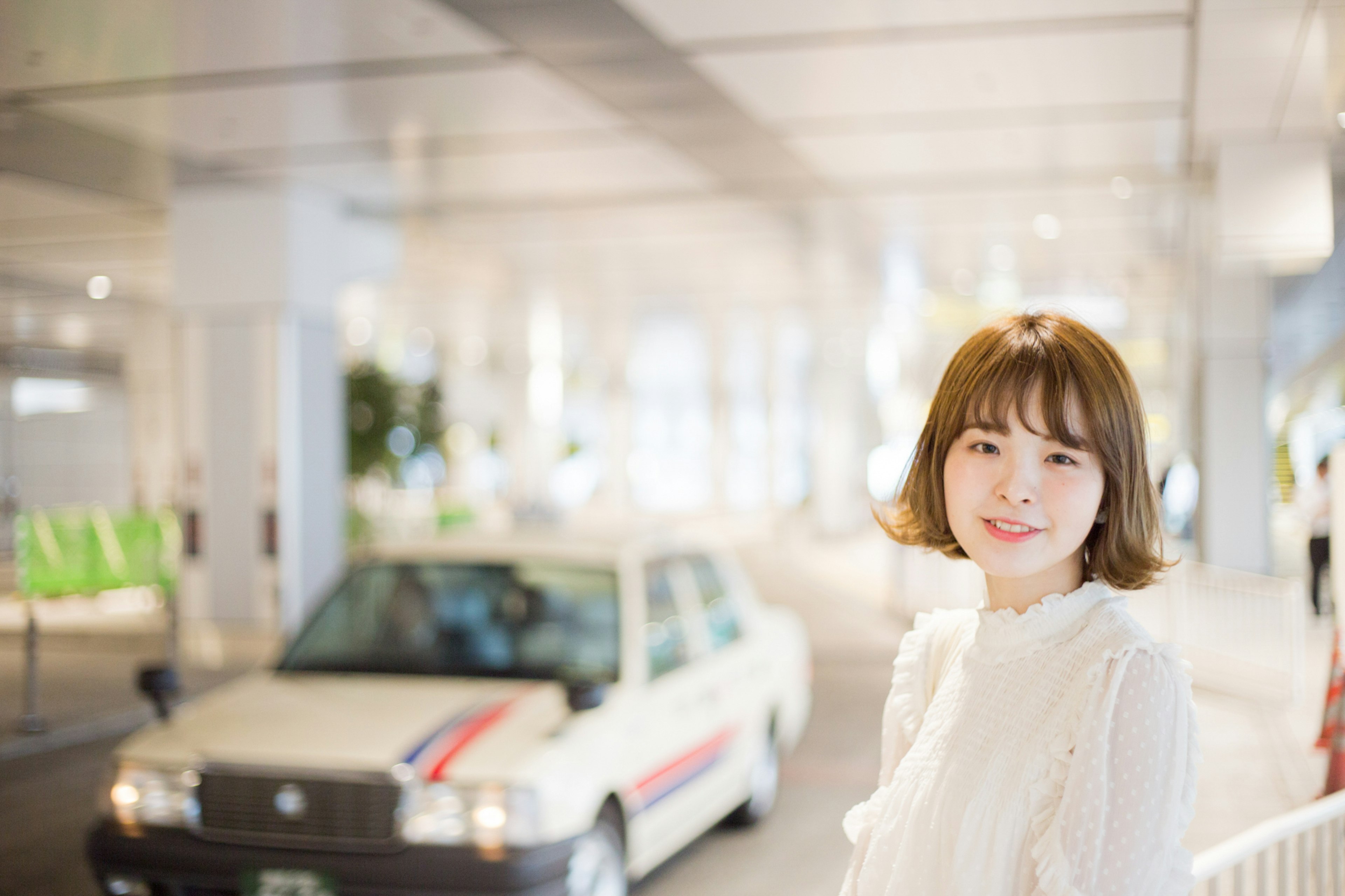 A woman in a white outfit smiling with a taxi in the background