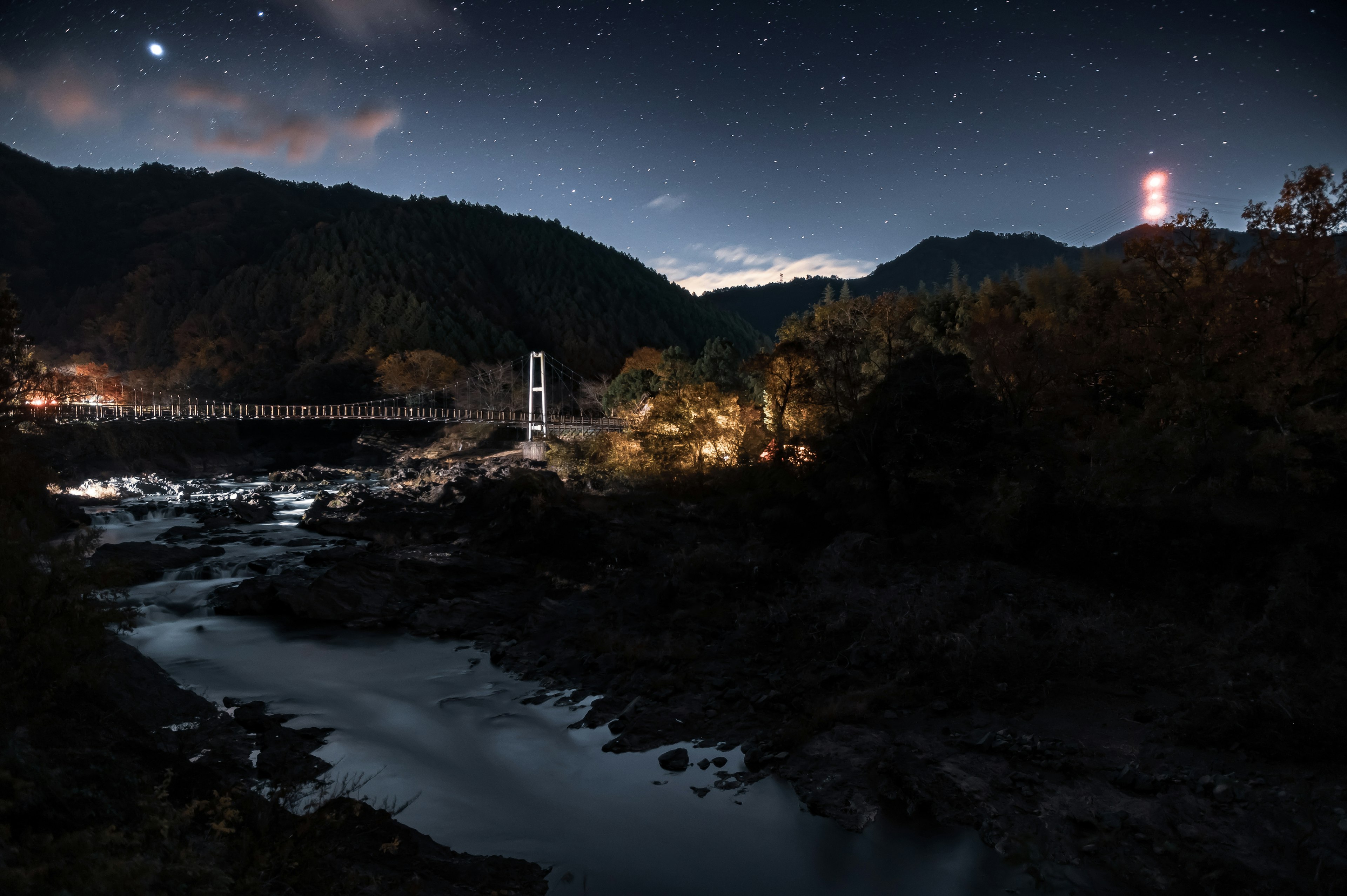 Vista panoramica di un fiume e montagne sotto un cielo stellato con luci notturne brillanti