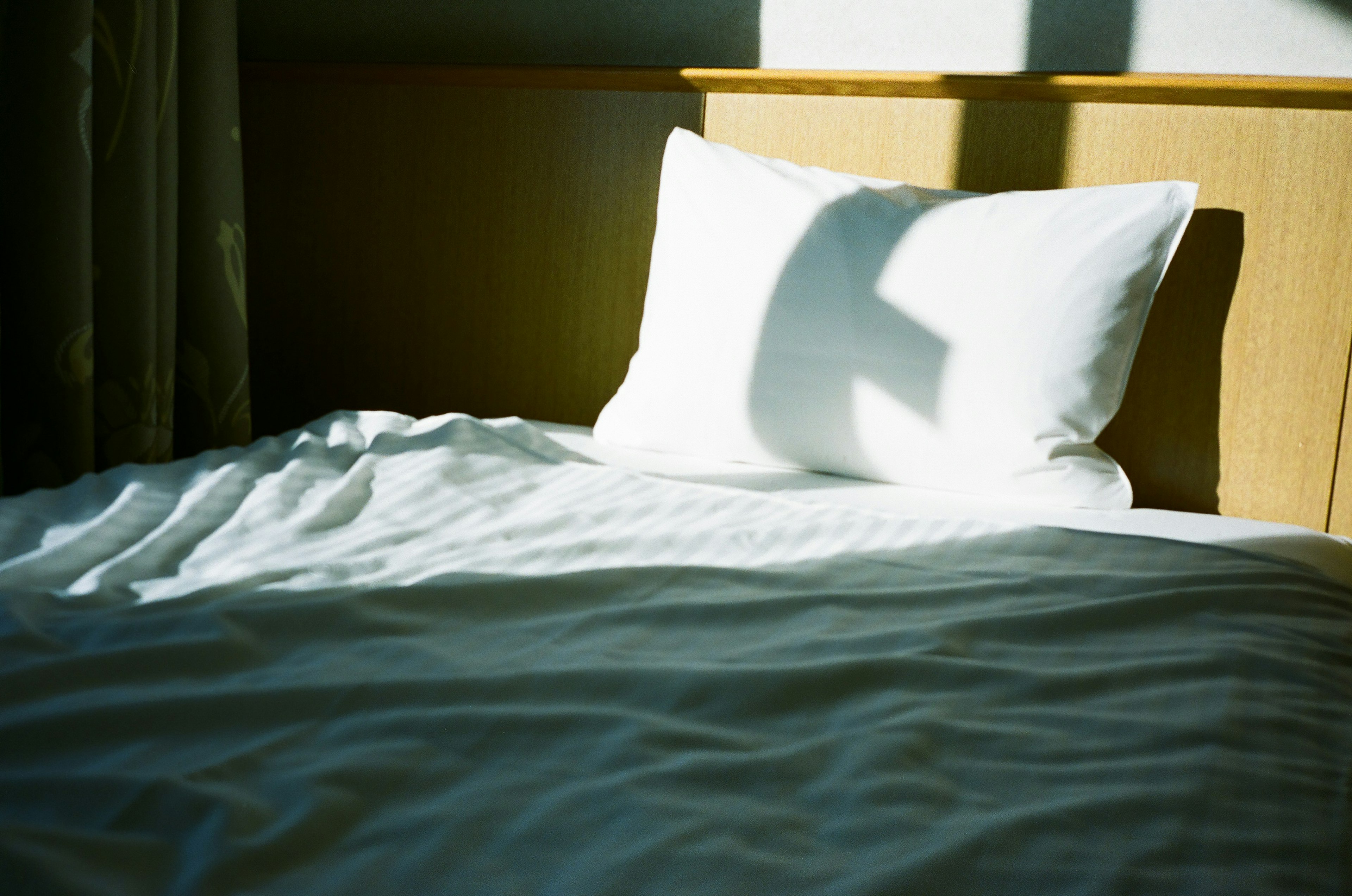 Close-up of a bed with white sheets and a pillow sunlight creating a shadow