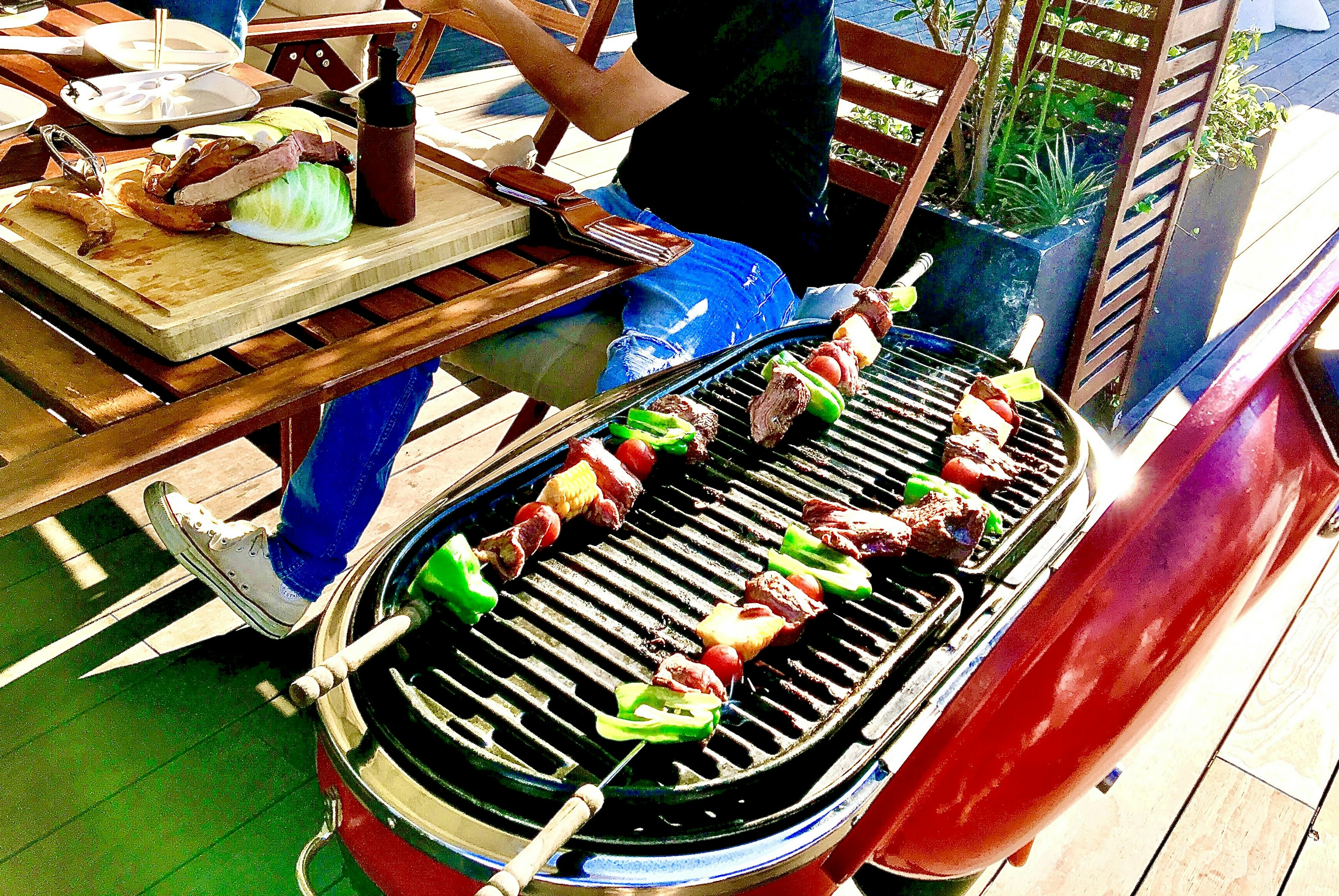 Colorful skewers grilling on a barbecue with a dining table nearby