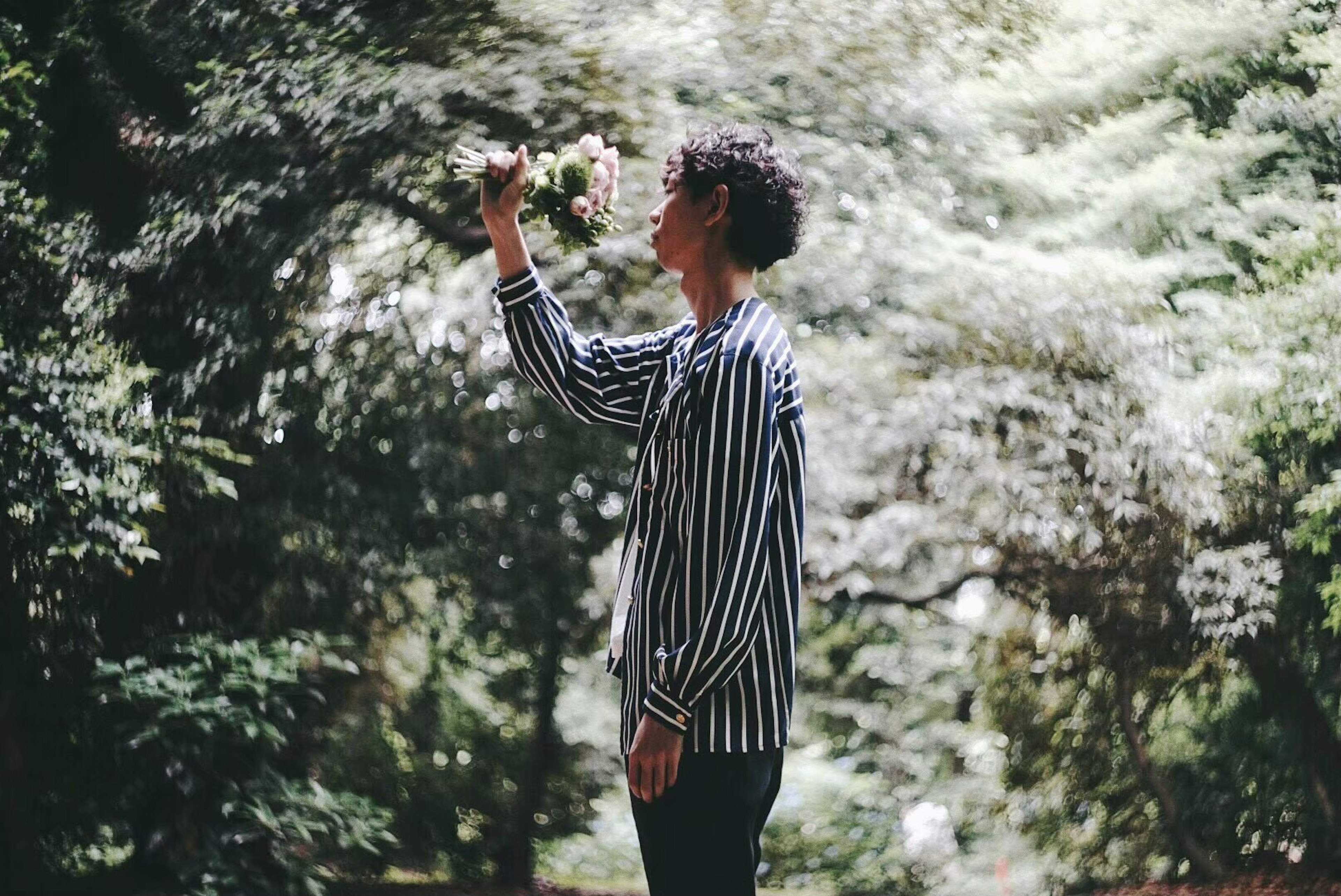 Giovane uomo in camicia a righe che tiene un fiore in piedi in una foresta