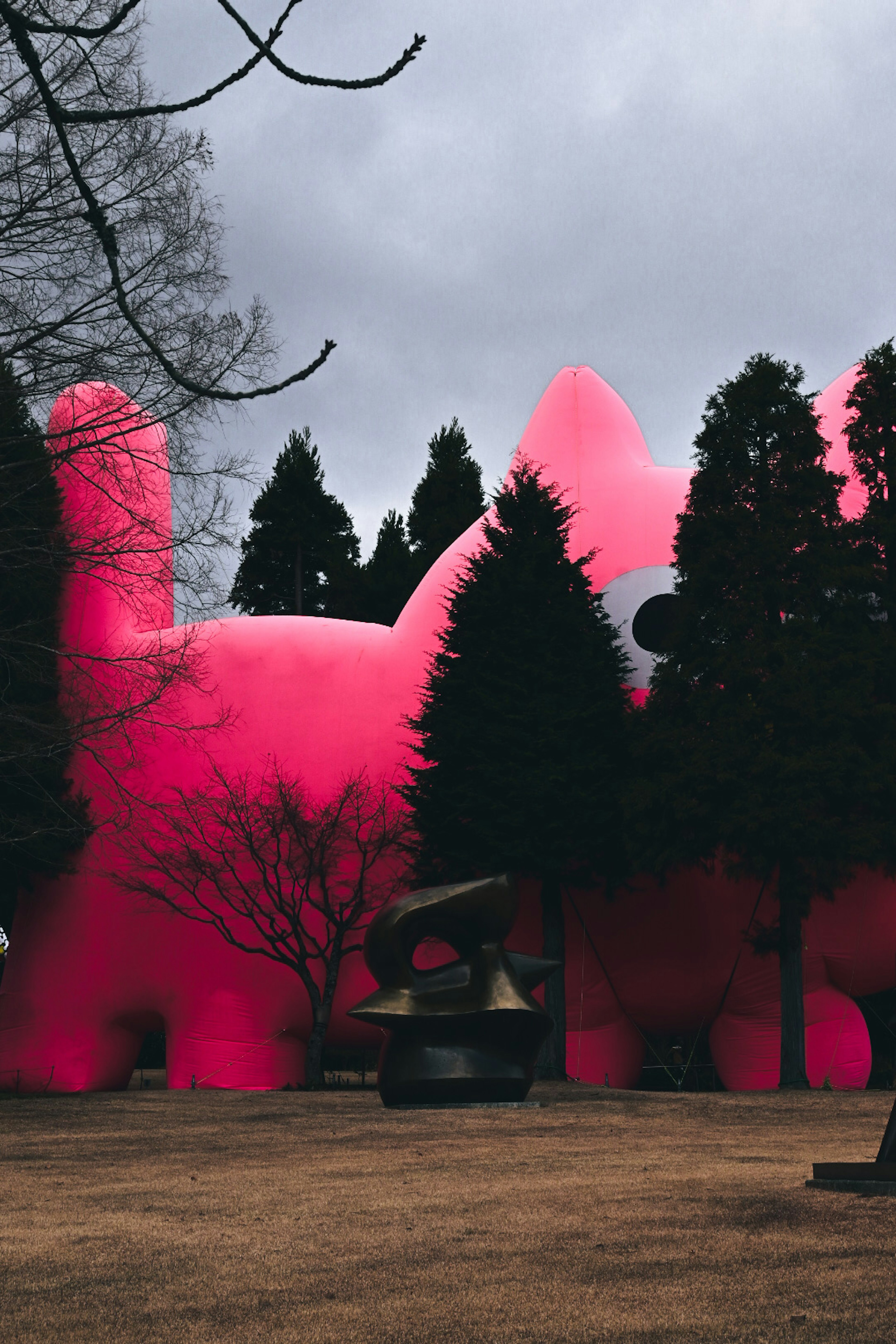 Une grande sculpture de chat rose se cache derrière des arbres dans un parc