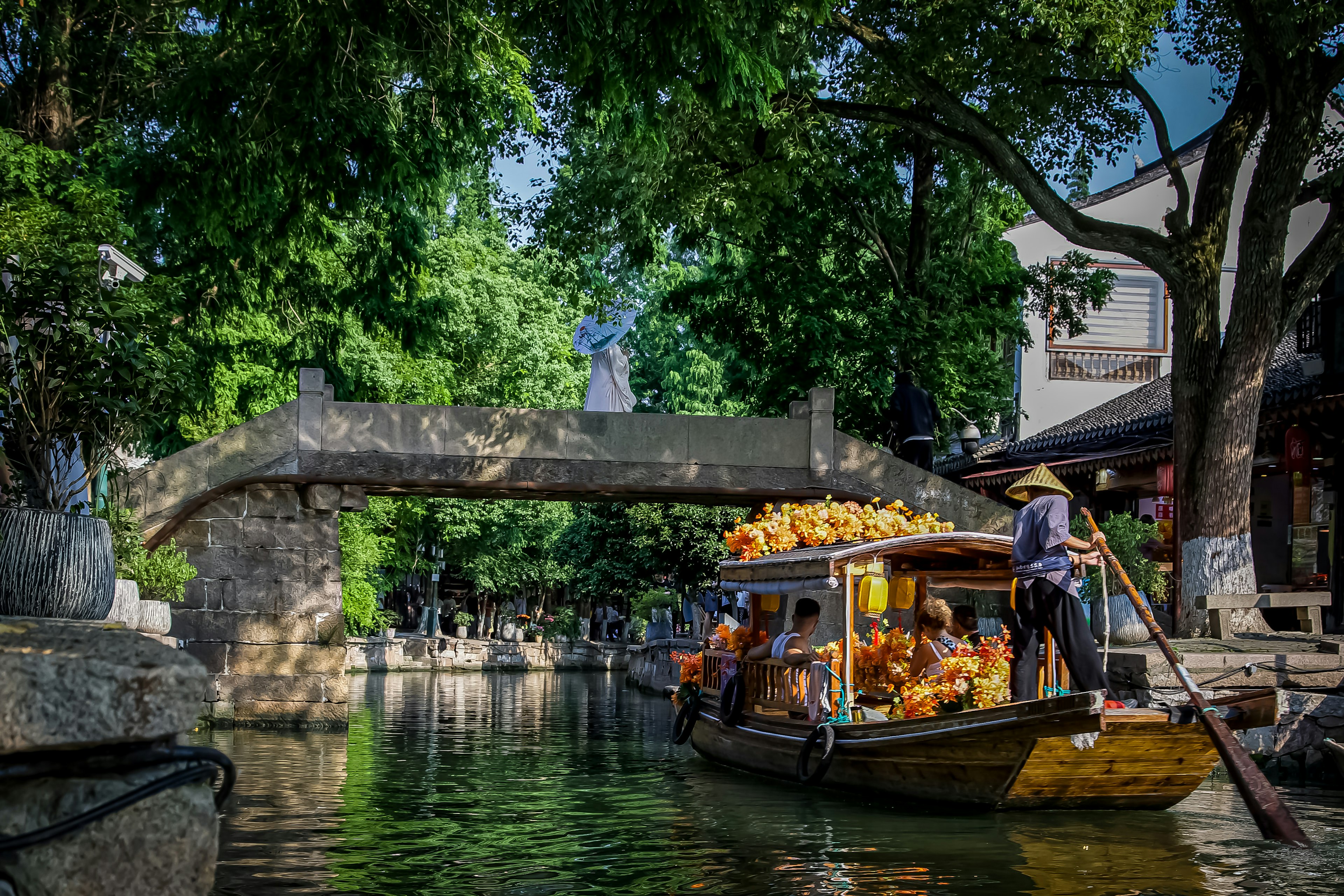 Scenic canal with a boat carrying goods under a stone bridge surrounded by lush greenery