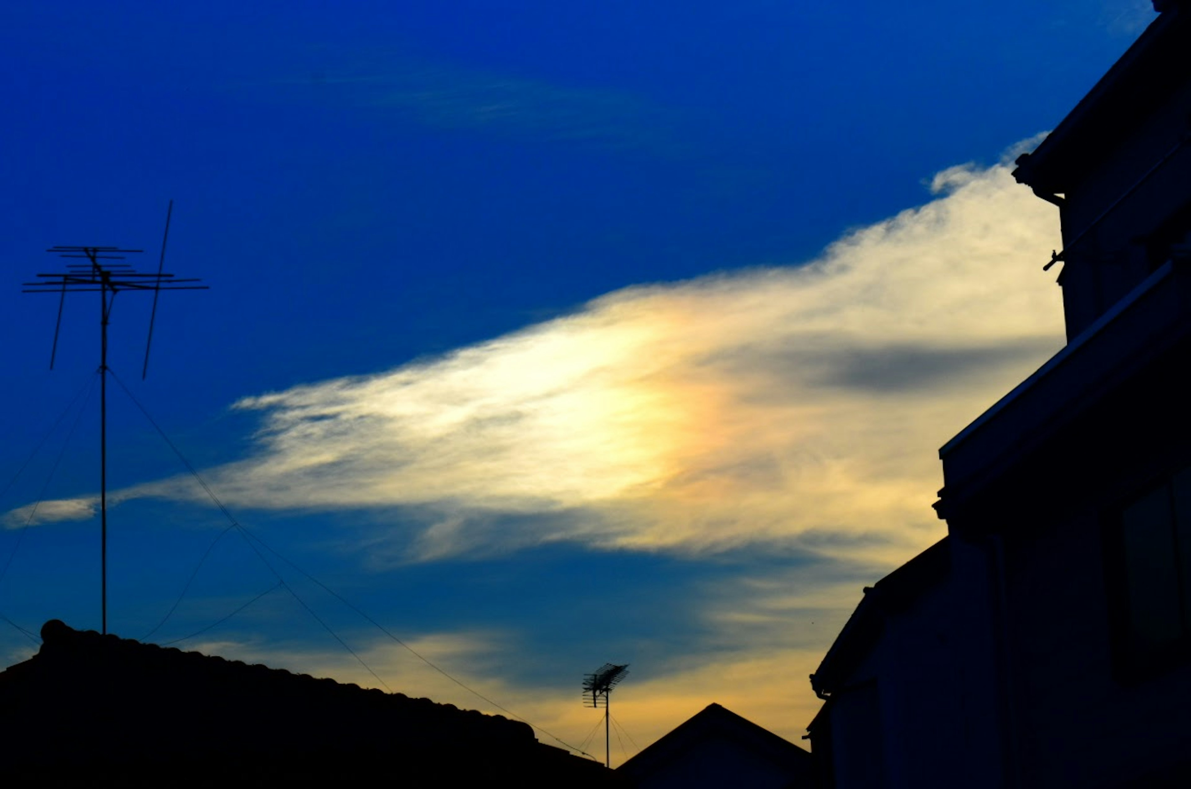 Ein Sonnenuntergangshimmel mit blauen Nuancen und weißen Wolken, silhouettiert gegen Dächer