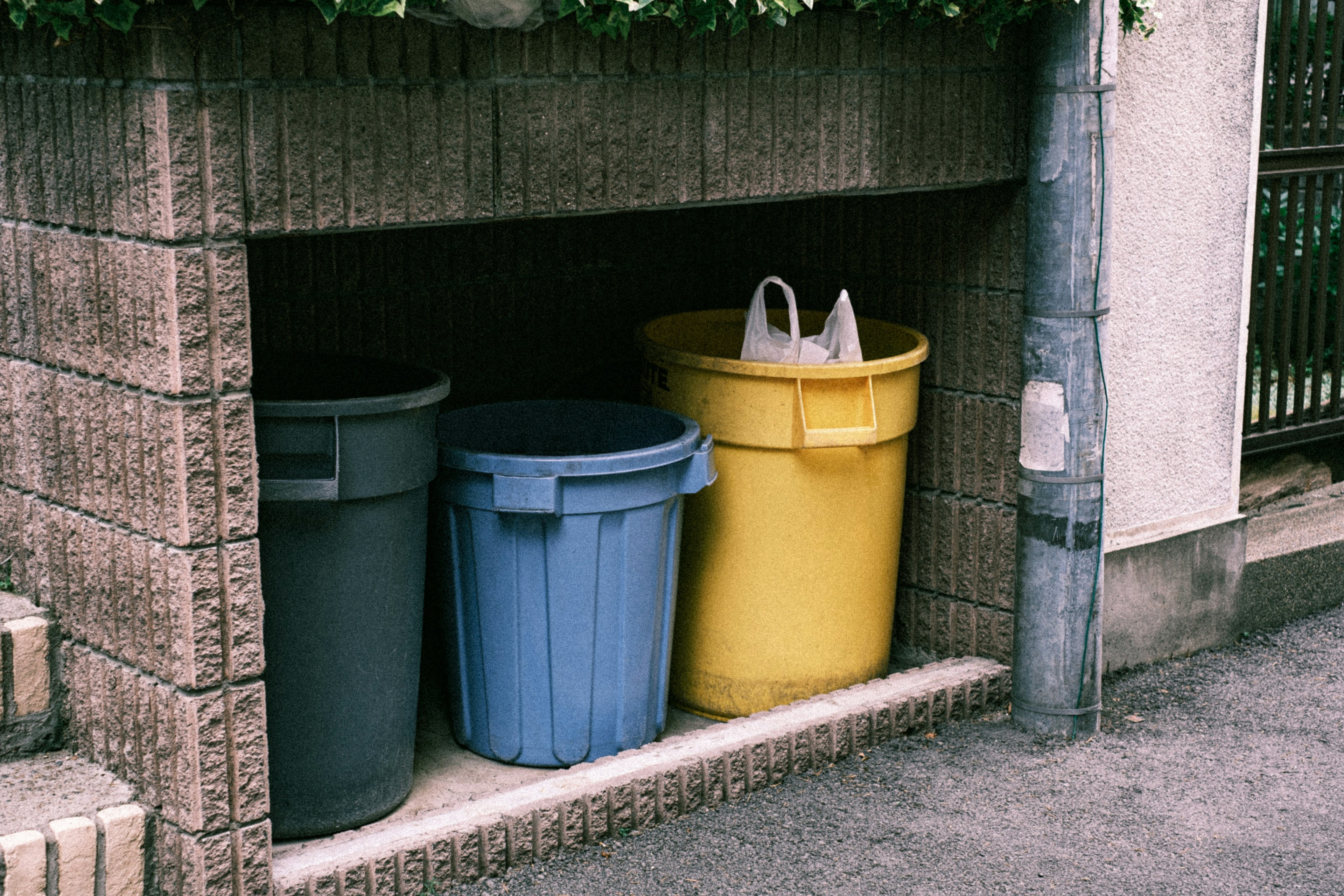 Trois poubelles colorées alignées dans un coin de rue