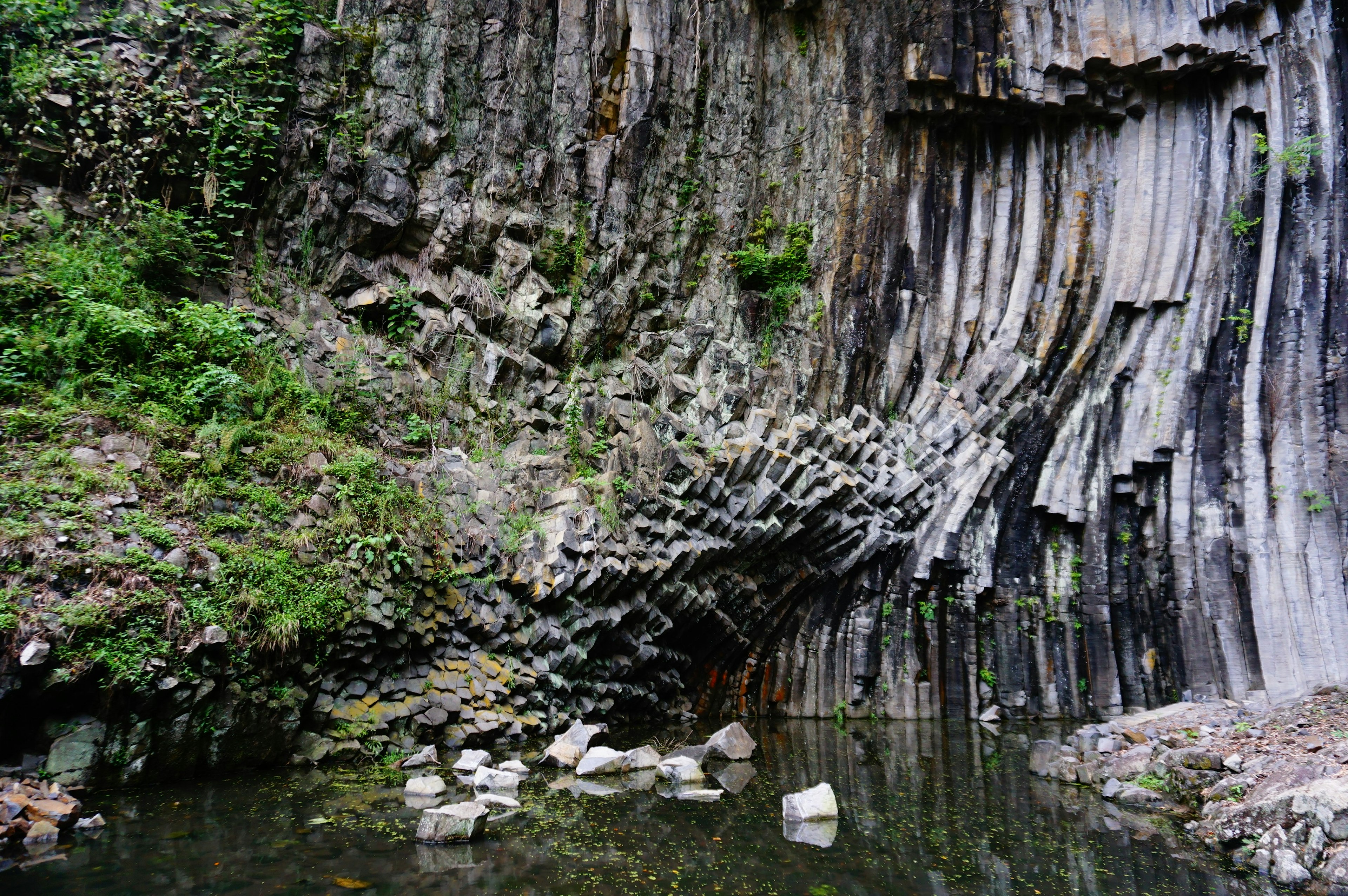 Natural landscape featuring columnar basalt formations and reflections in water