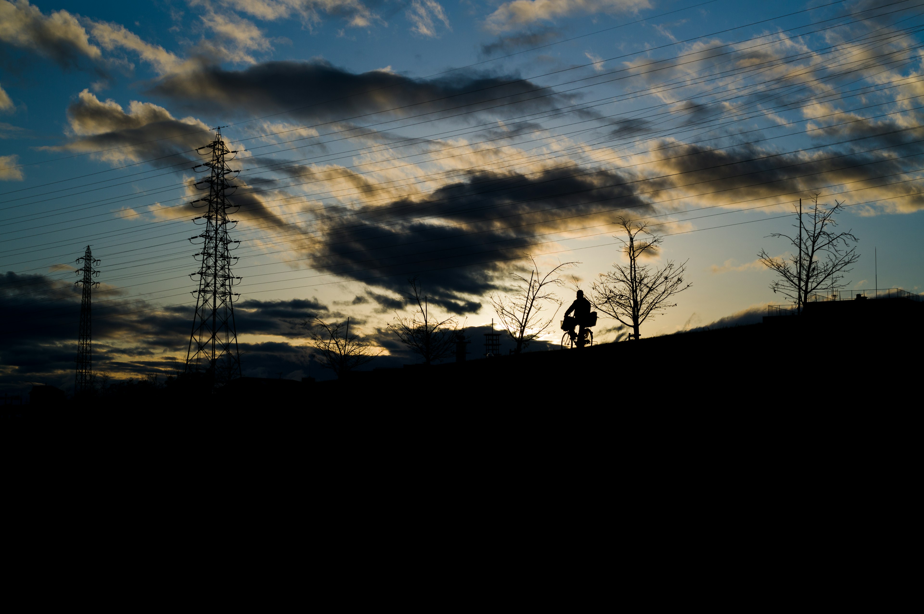 夕焼けの中、シルエットの人物が丘を歩いている風景