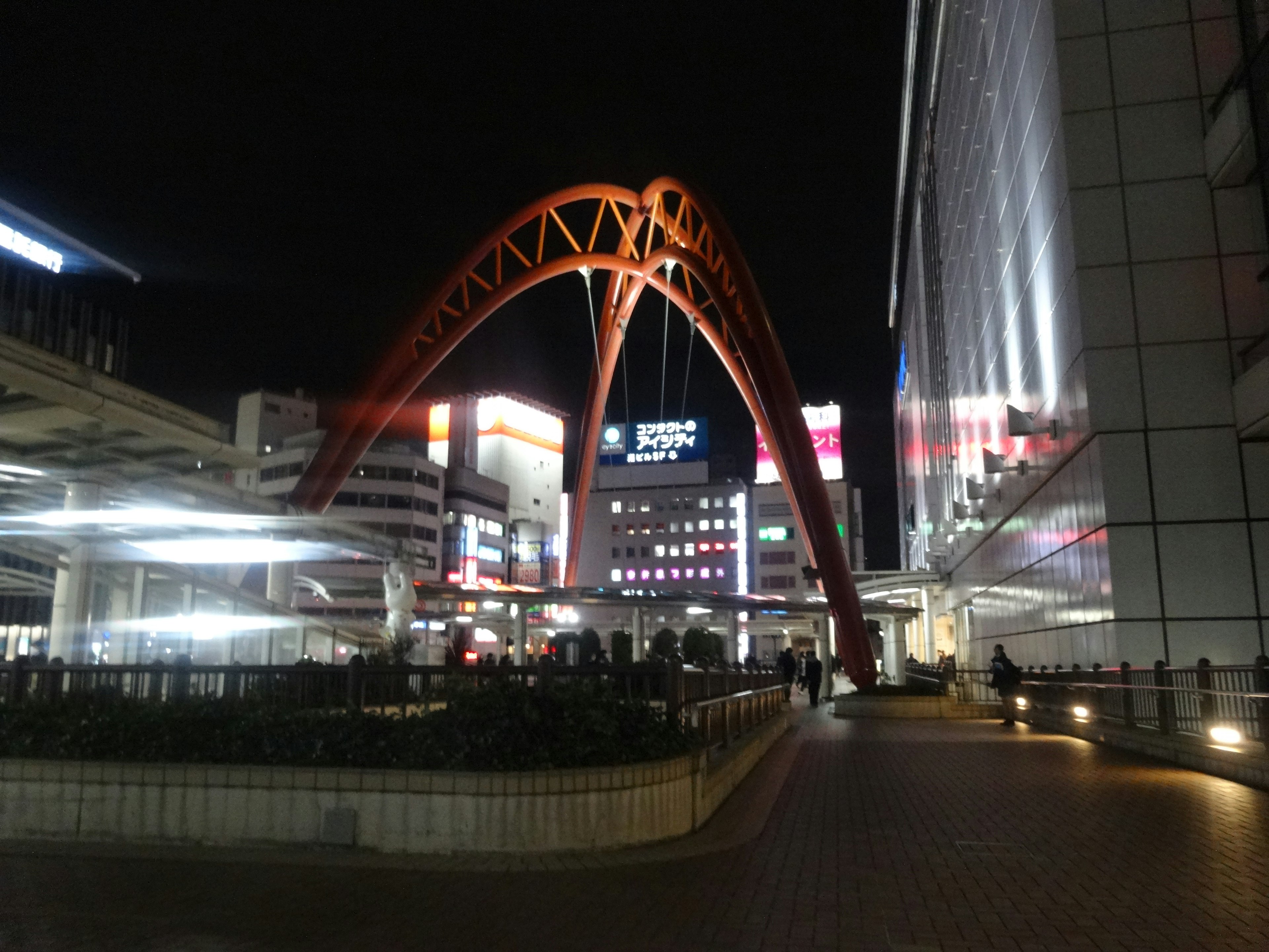 Prominent orange arch structure illuminated at night with surrounding buildings