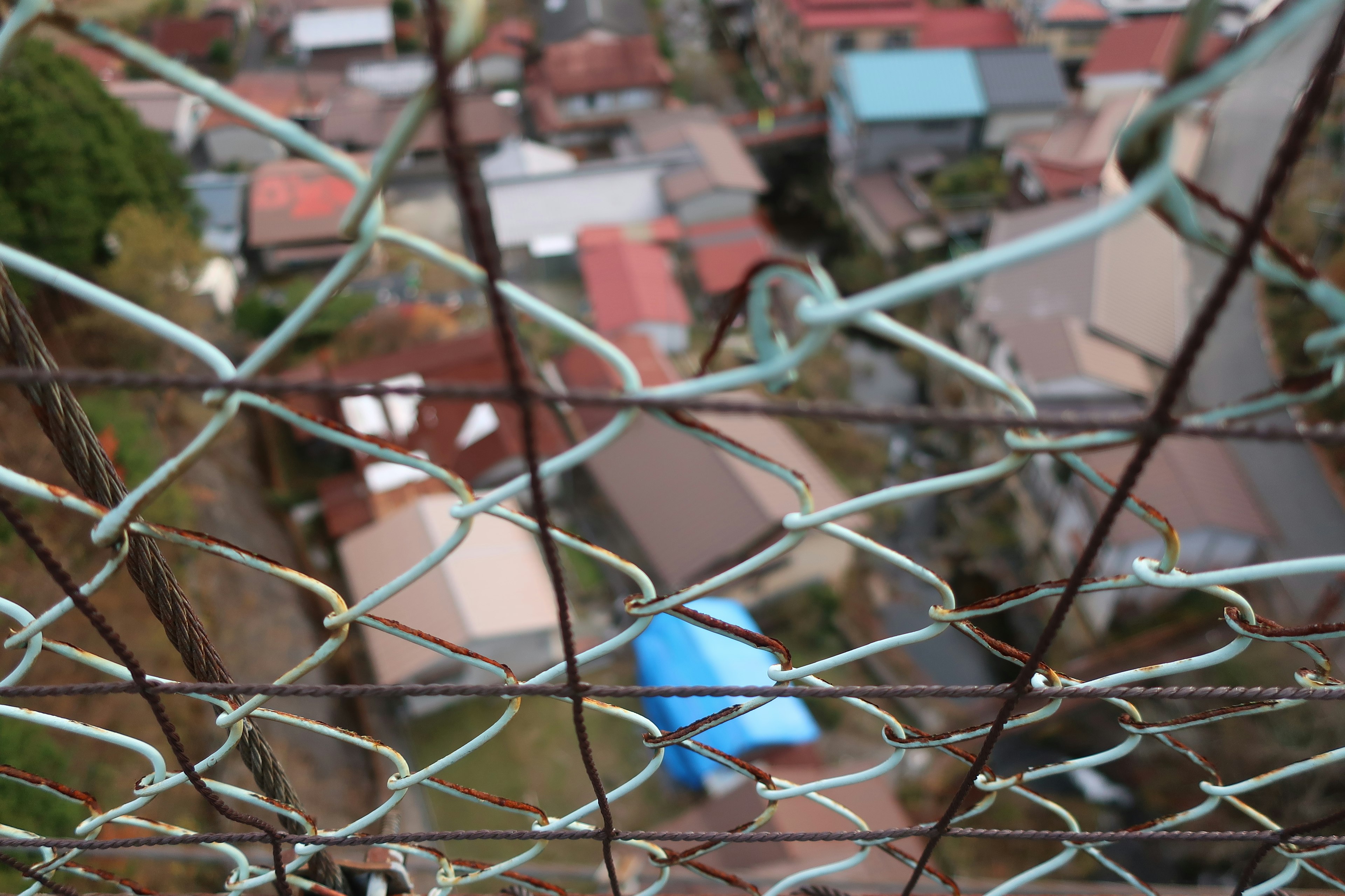 A view of a residential area through a fence featuring blue and red roofs