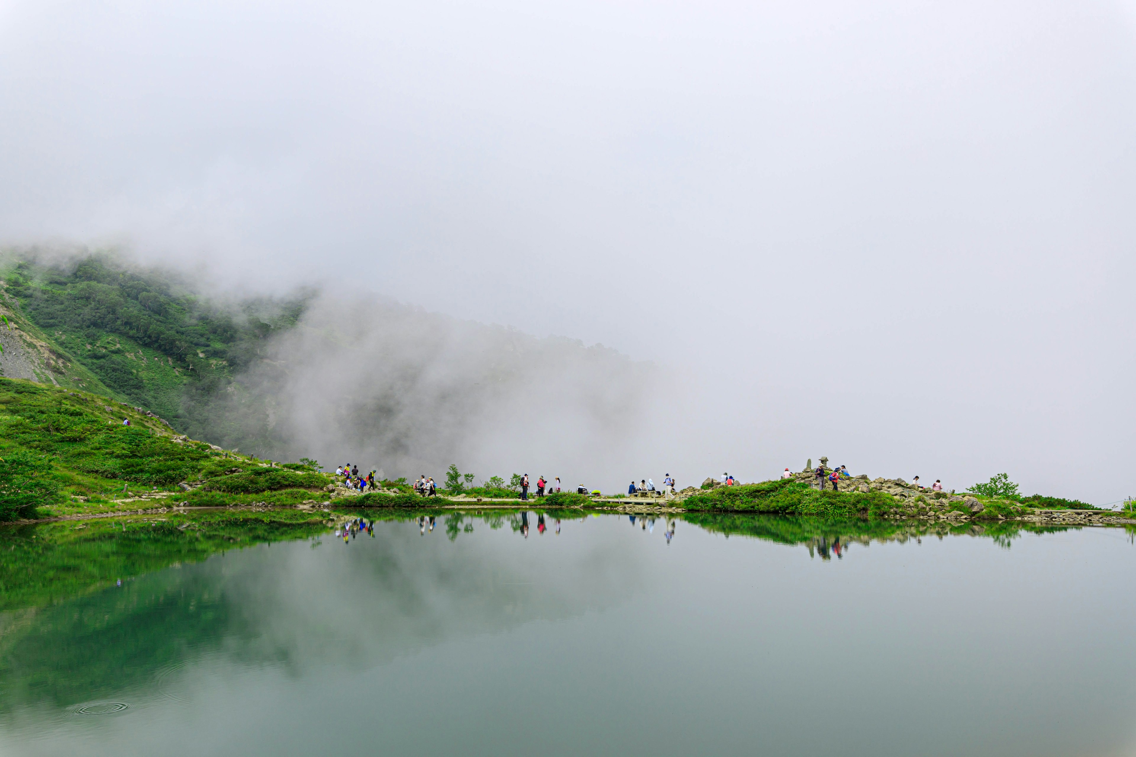 Misty mountain landscape with a calm lake and people in the distance