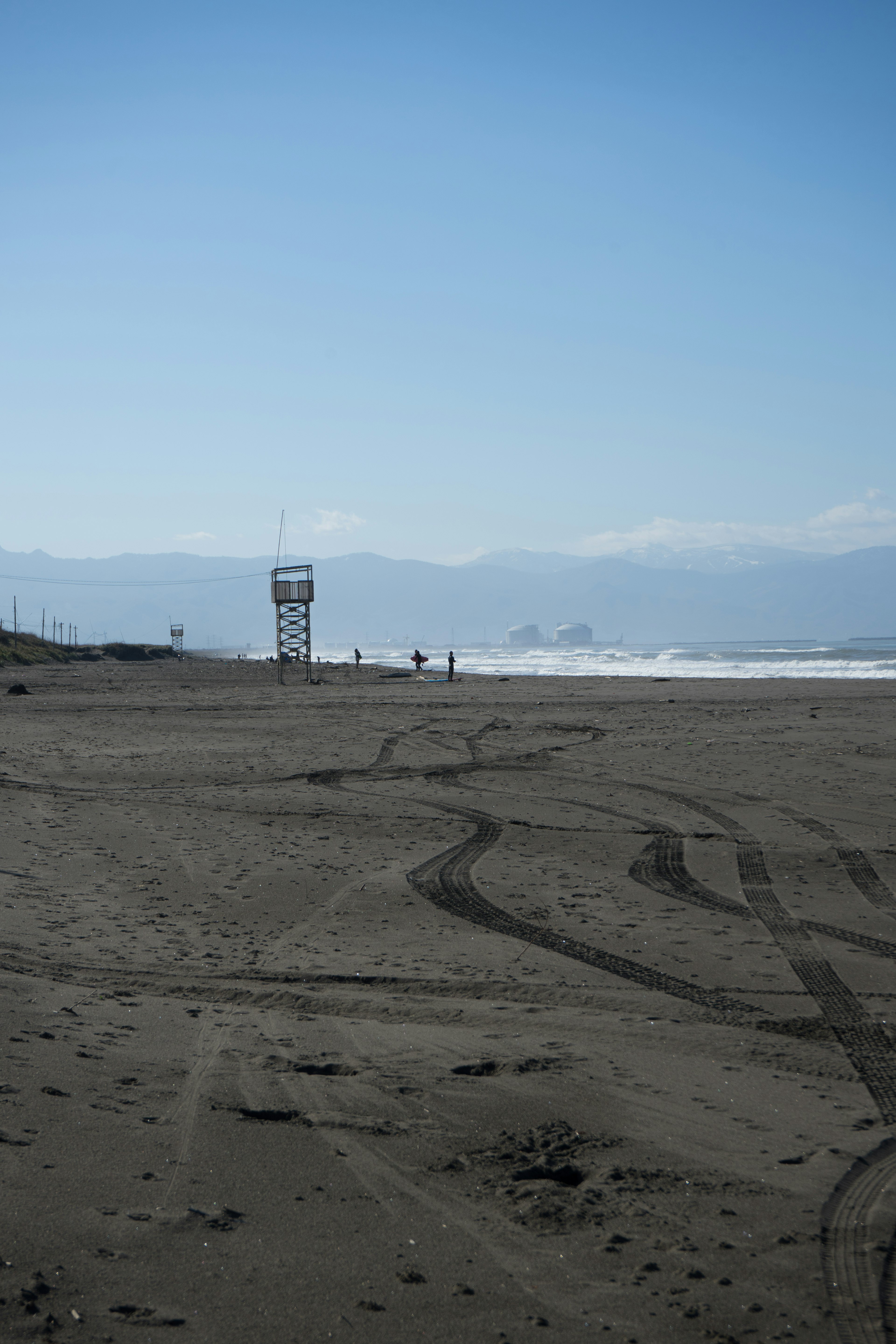 Scène côtière avec une tour de sauvetage et une plage de sable sous un ciel bleu et des montagnes au loin