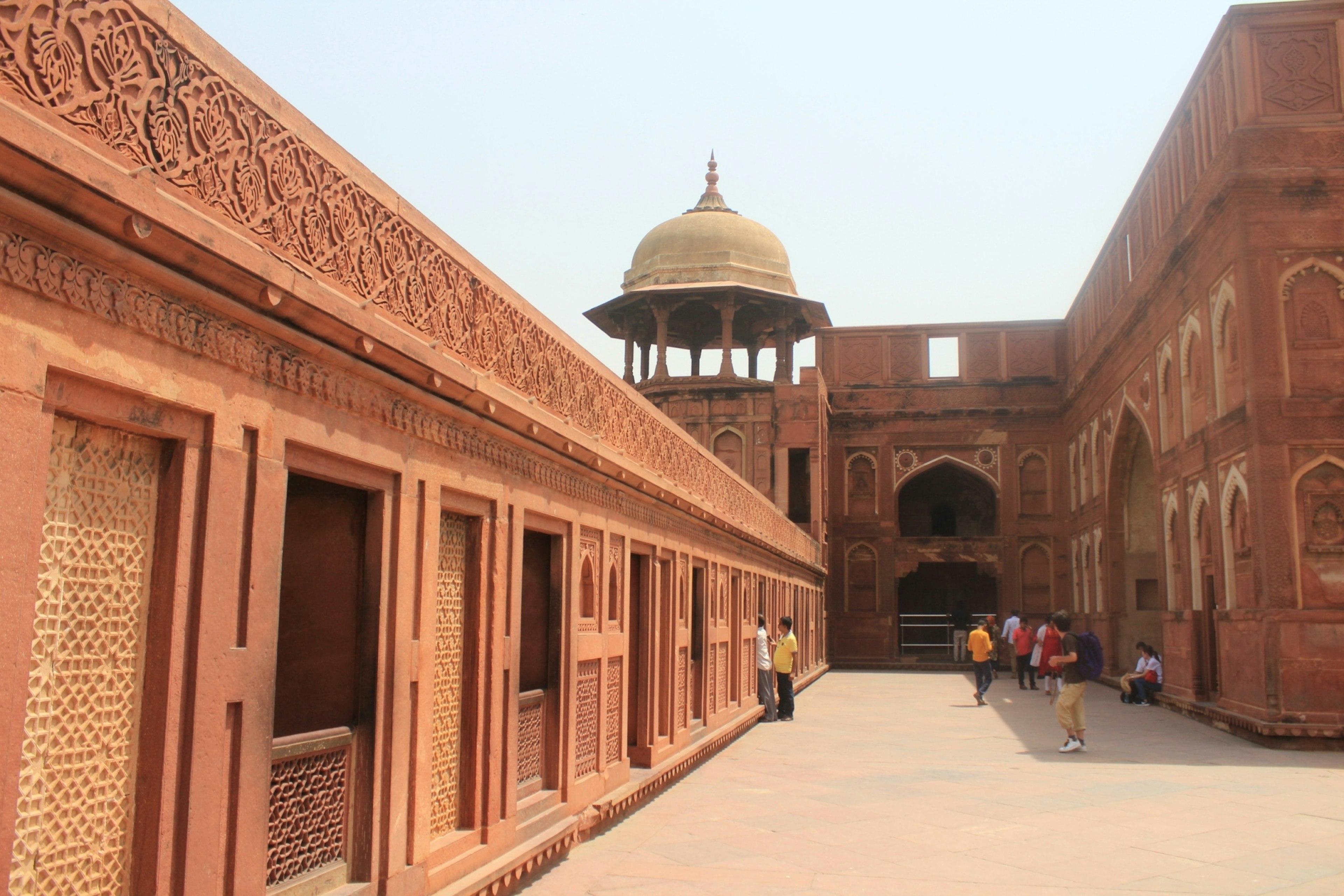 Red sandstone building with intricate carvings and archways in a courtyard