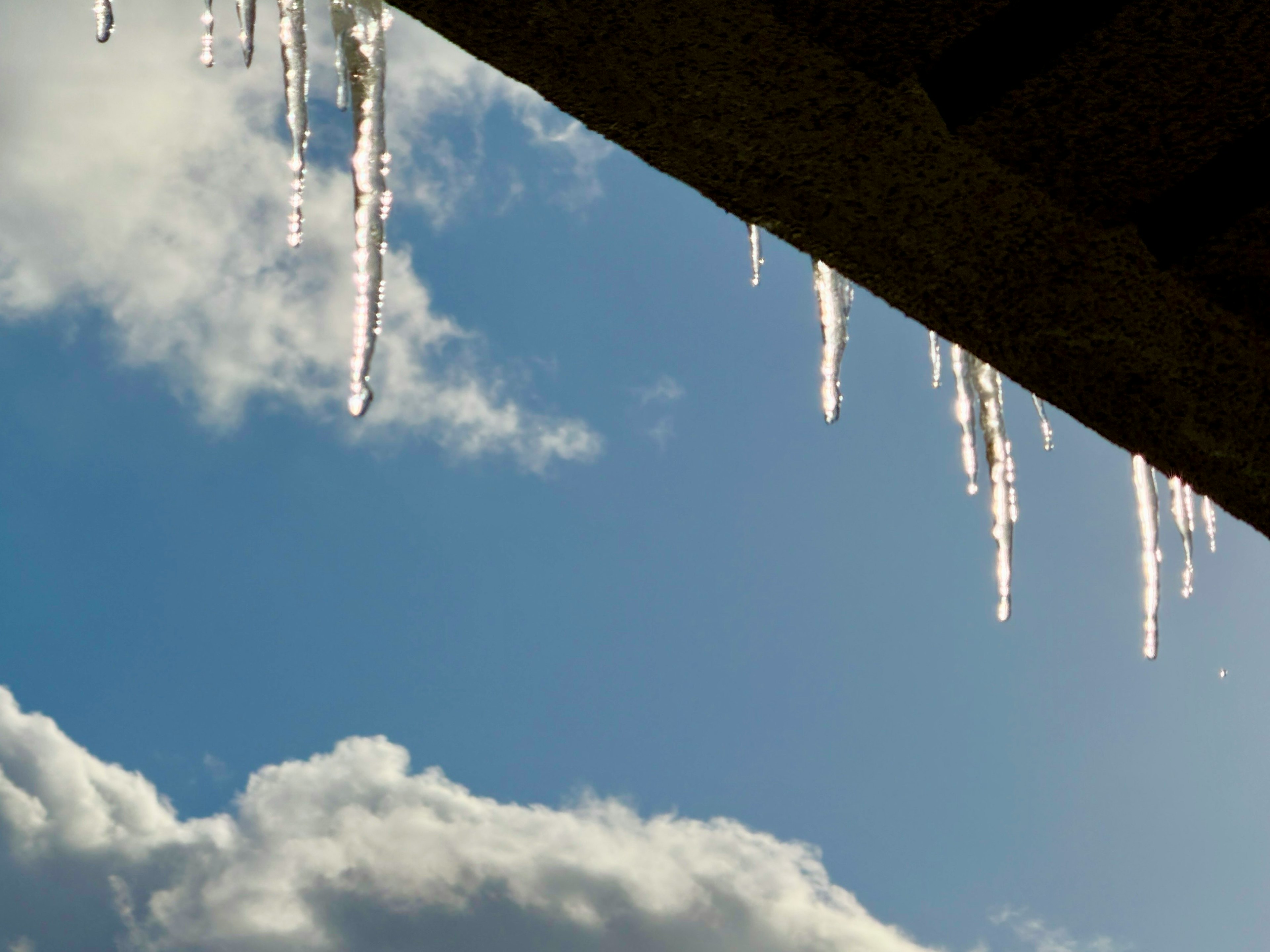 Icicles hanging under a roof against a blue sky