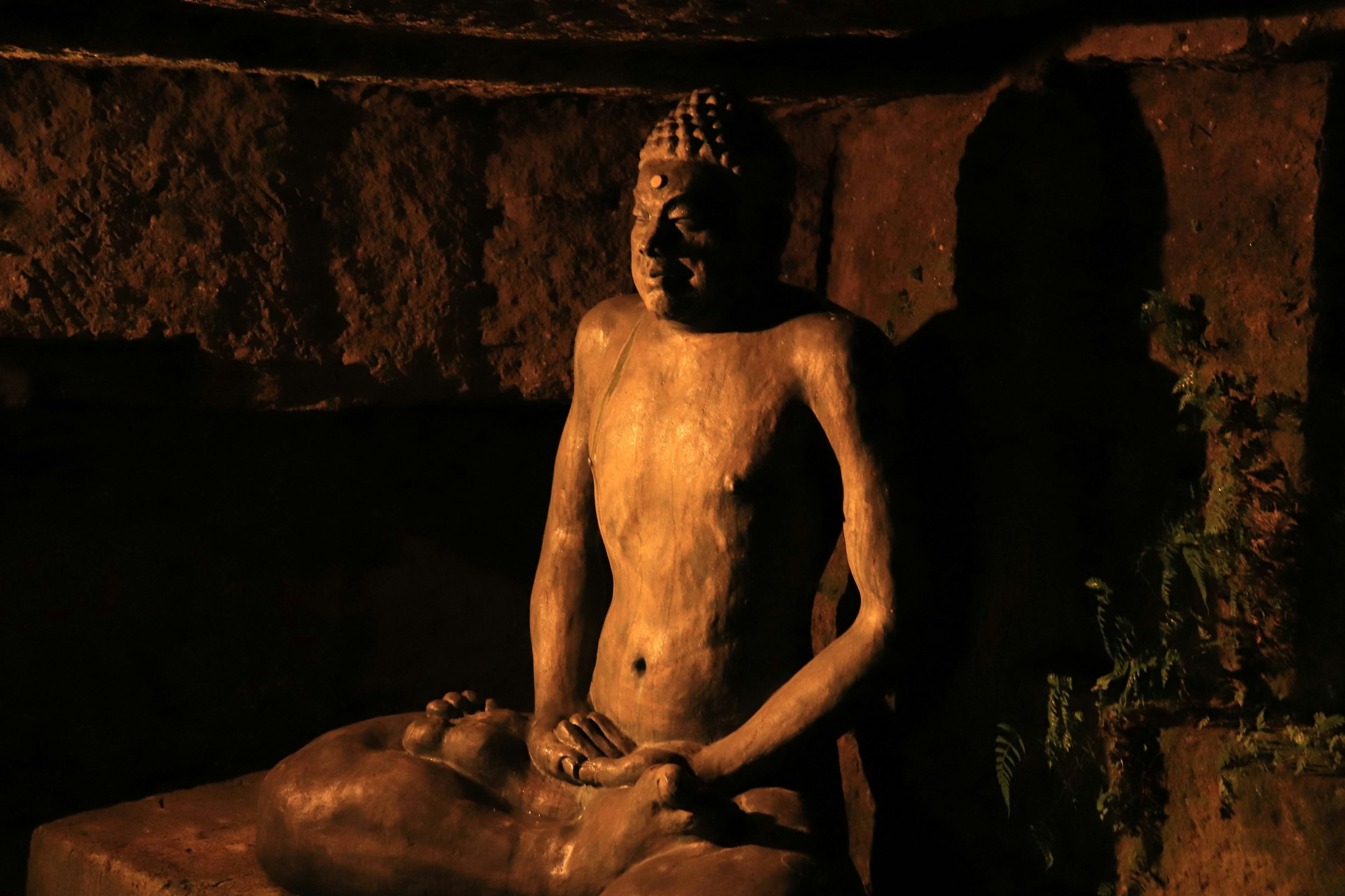 Image of a Buddha statue seated in a stone cave illuminated by dim light