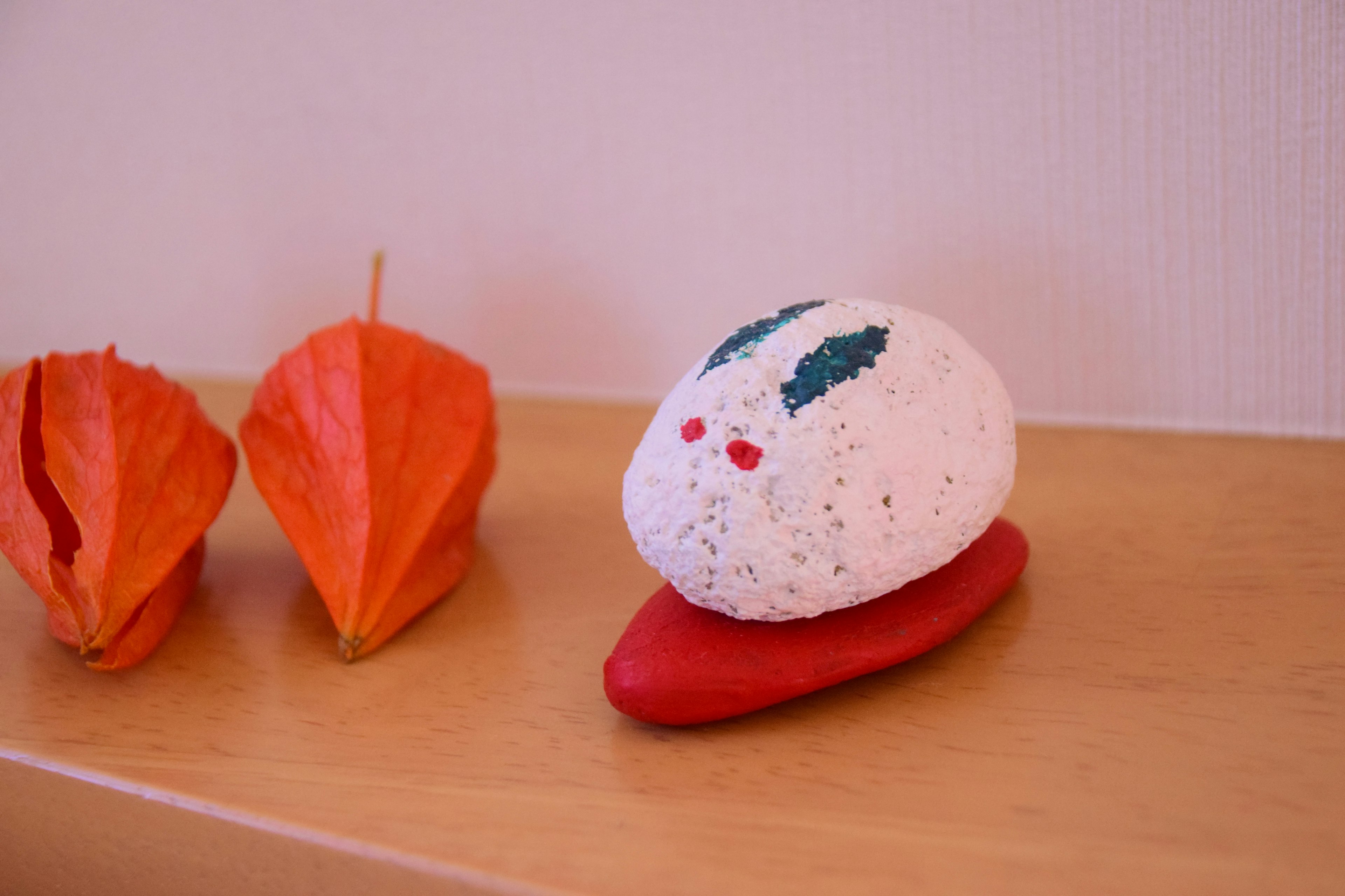 White stone figure with green leaves and red eyes on a red base next to orange leaves