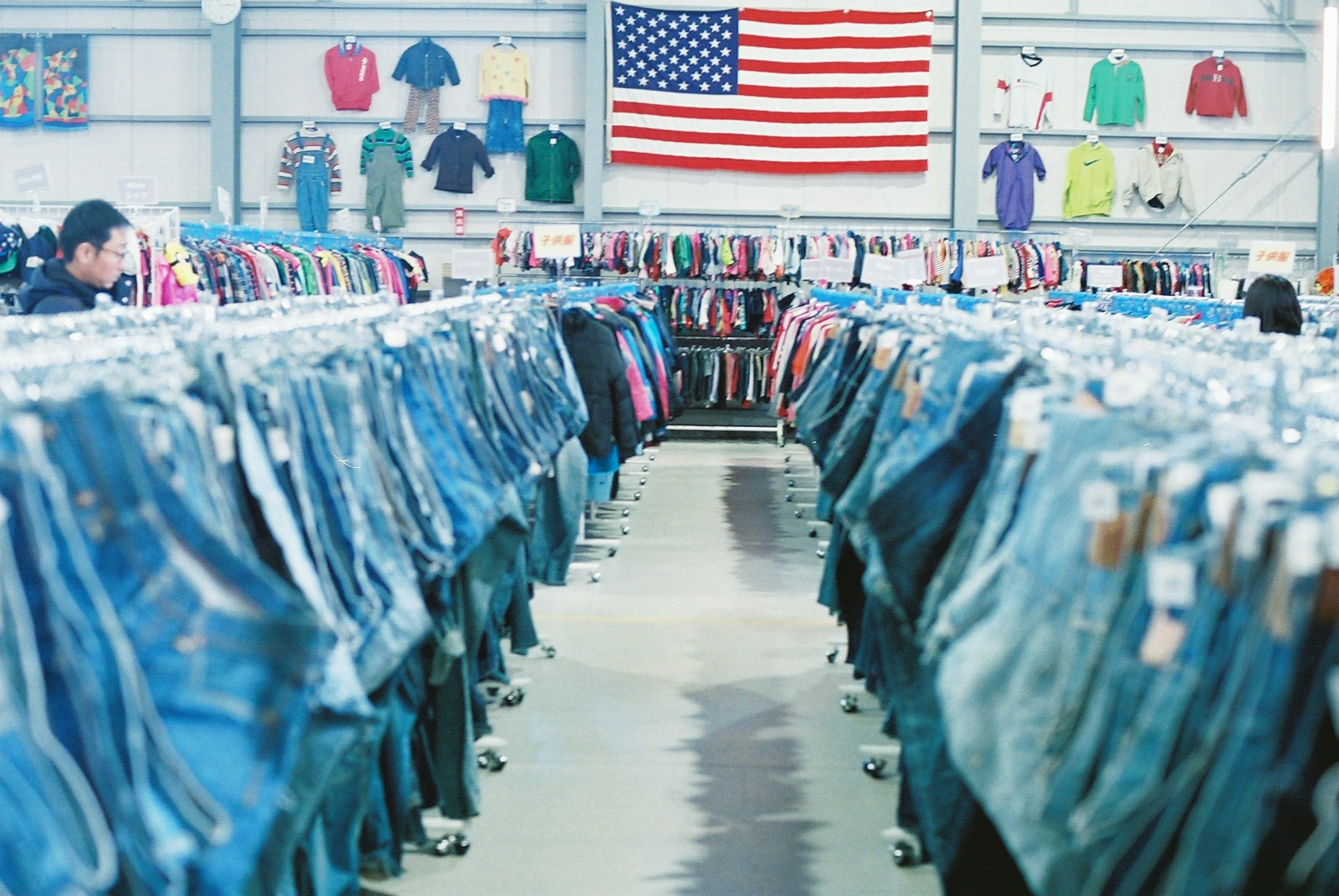 Interior de una tienda de segunda mano con filas de jeans azules bandera estadounidense al fondo