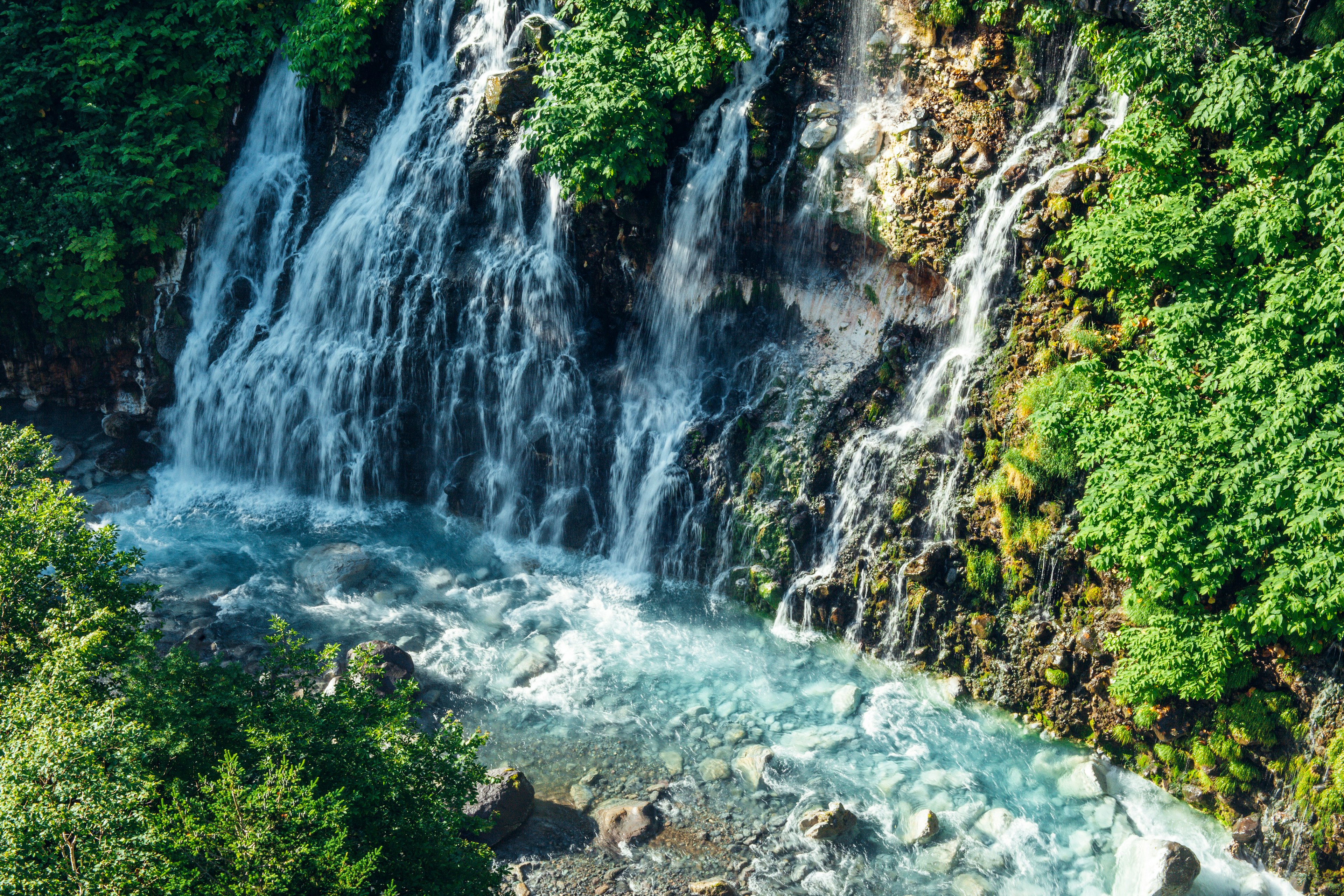 Air terjun indah dikelilingi pepohonan hijau subur dengan air biru jernih