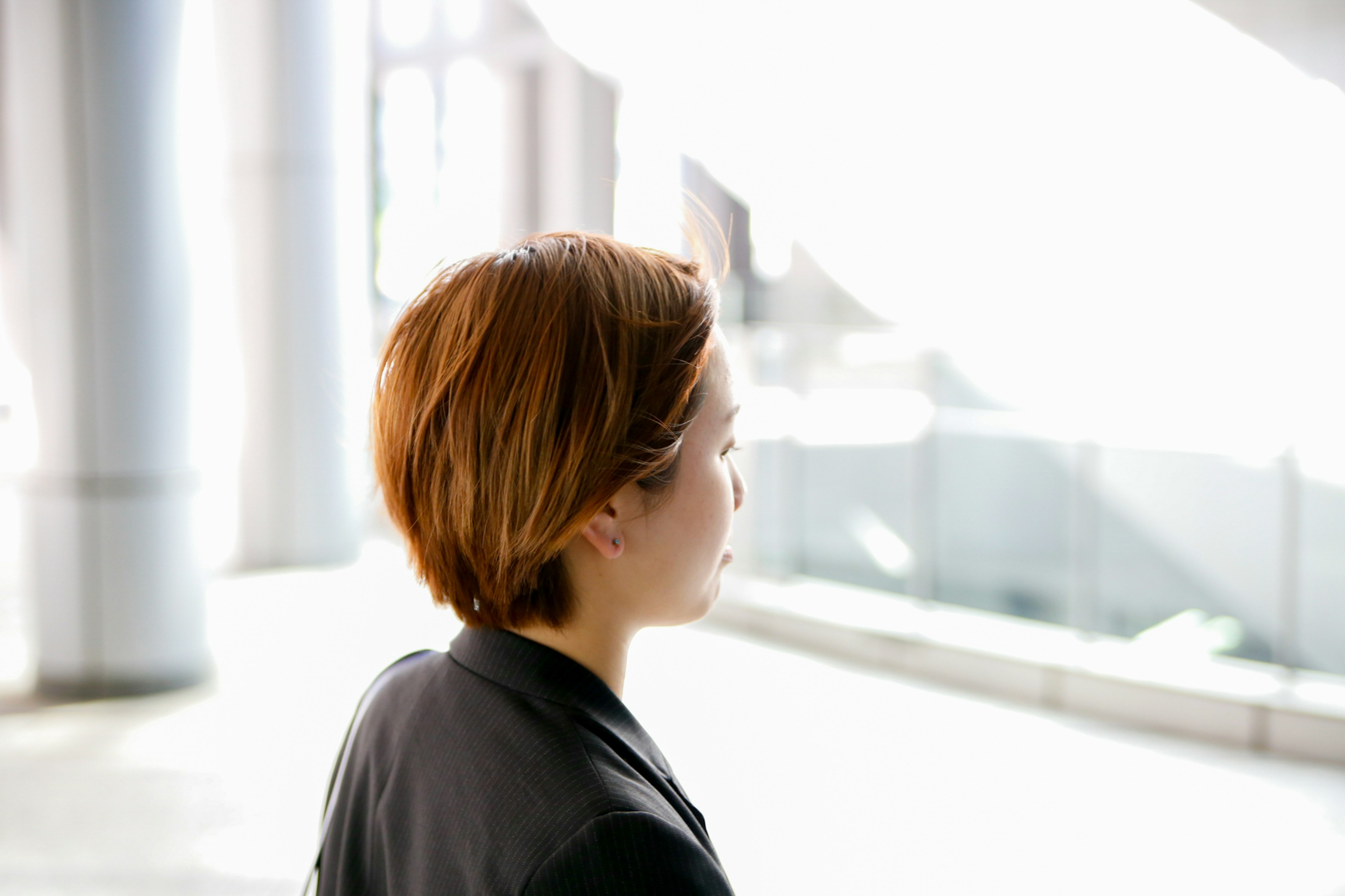 Profile of a woman looking away in a bright space with short brown hair wearing smart attire