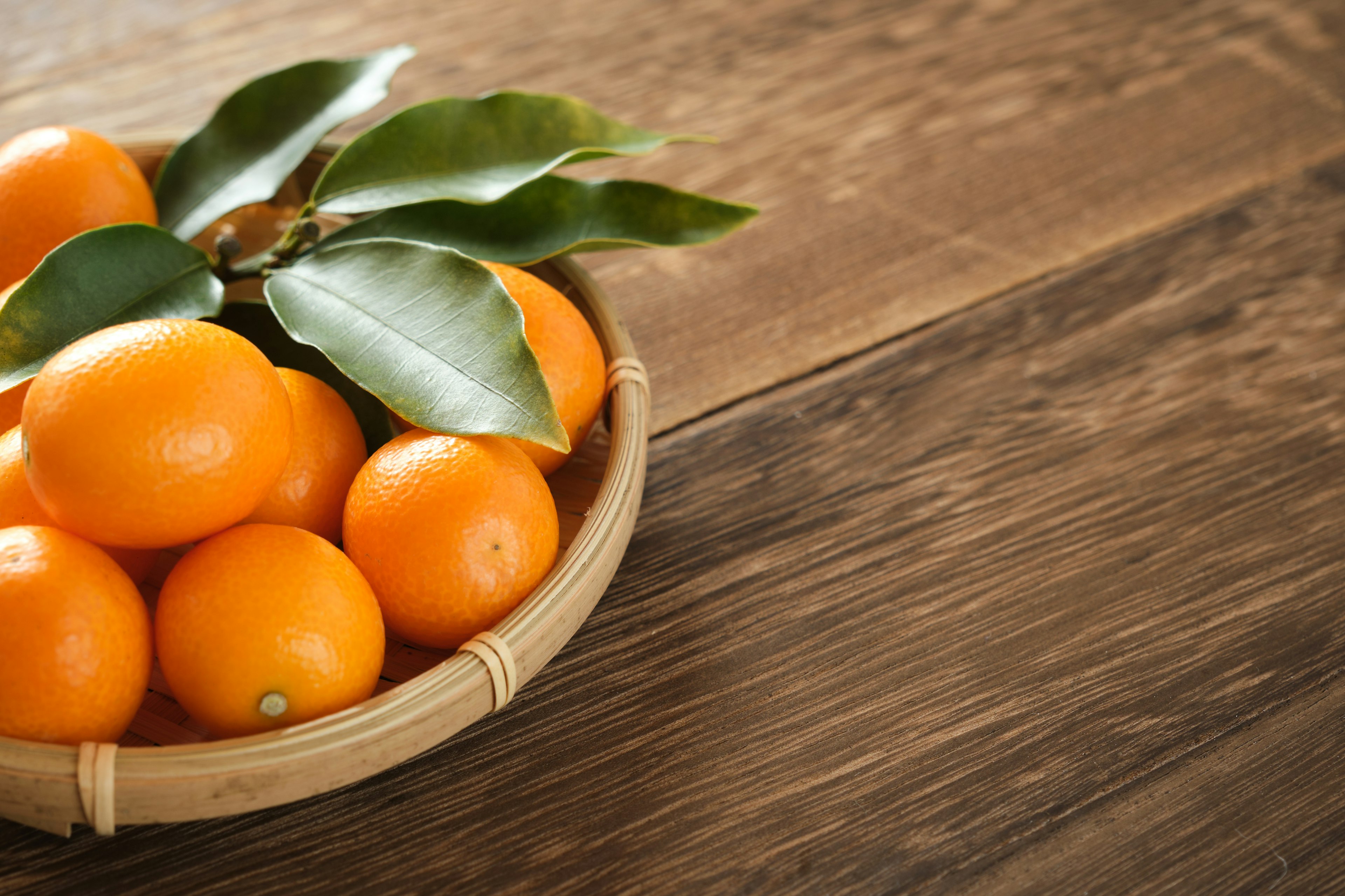 Cuenco de bambú lleno de fruta naranja sobre una mesa de madera