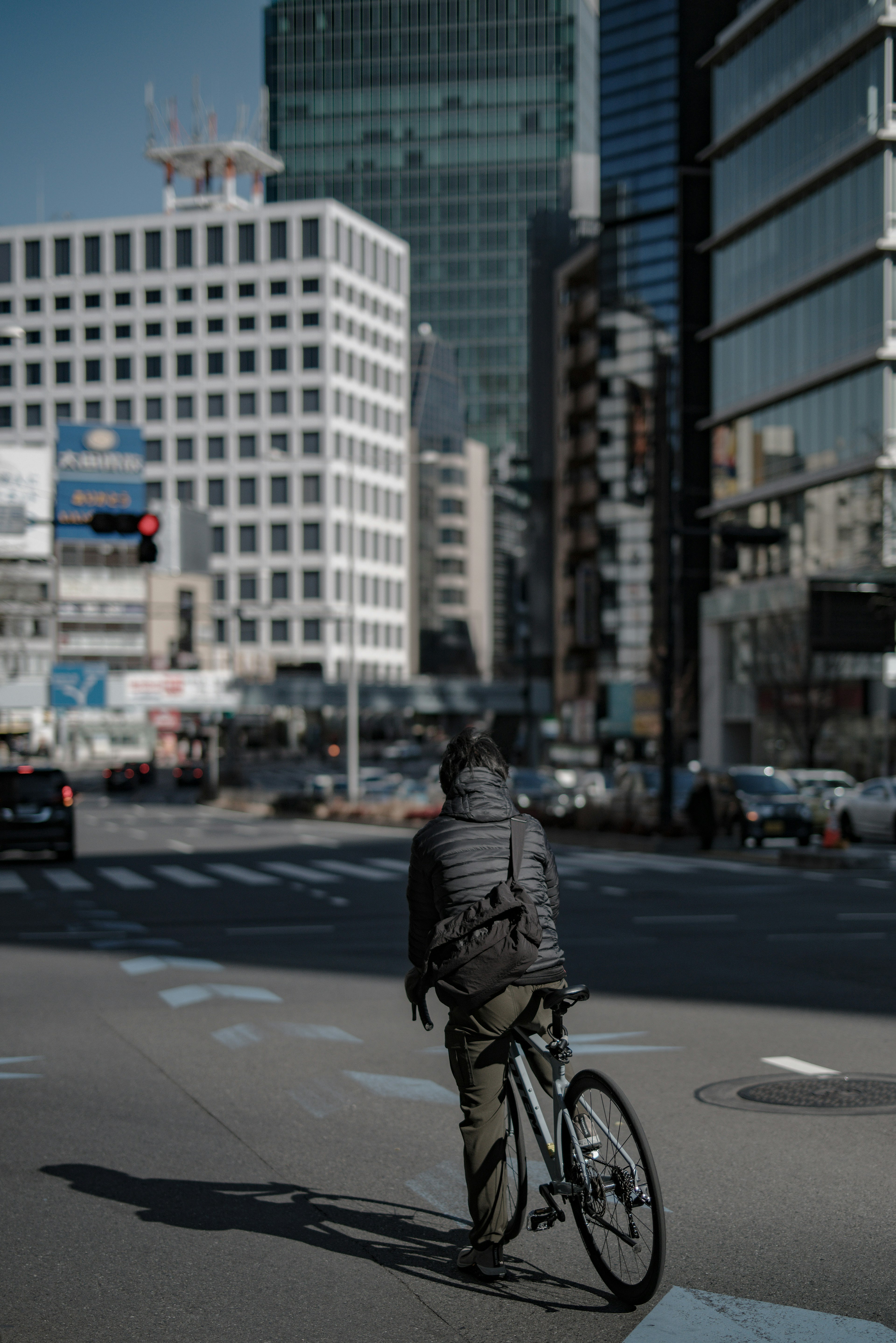 A person on a bicycle at an urban intersection with skyscrapers in the background