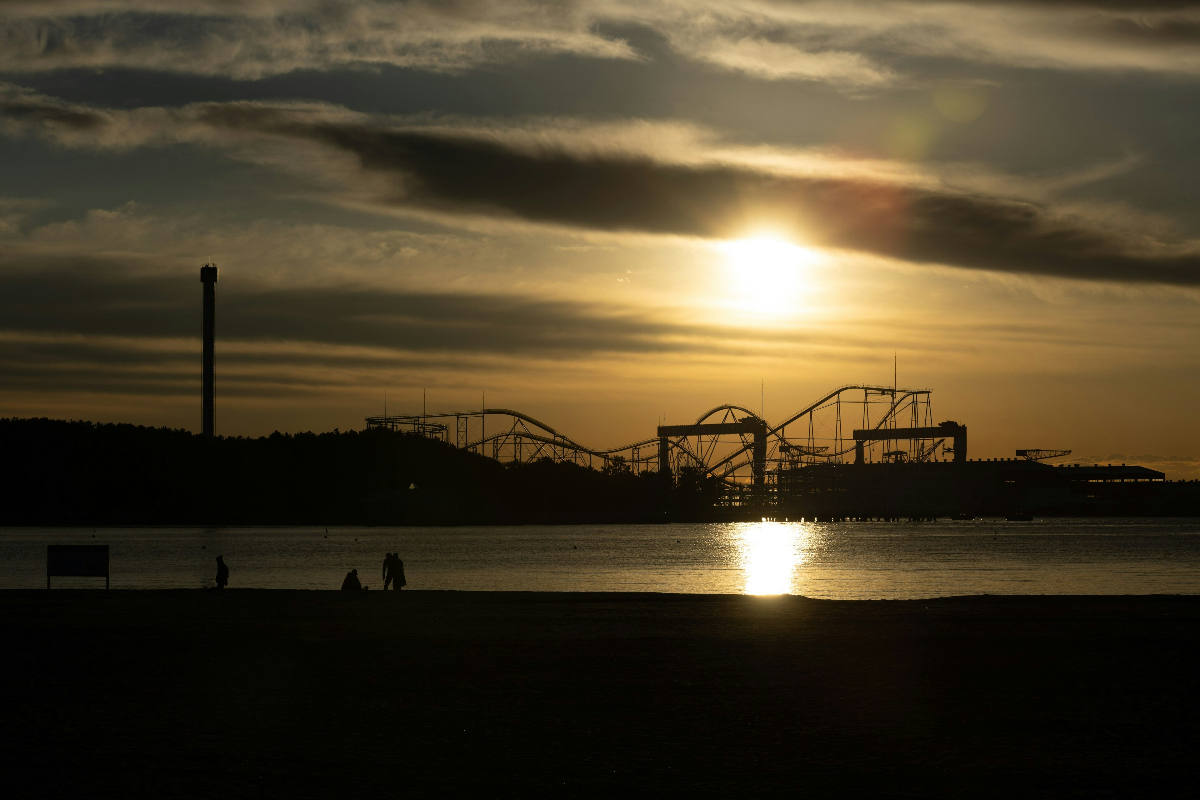 Silhouette von Achterbahnen eines Freizeitparks vor einem Sonnenuntergang über der Küste
