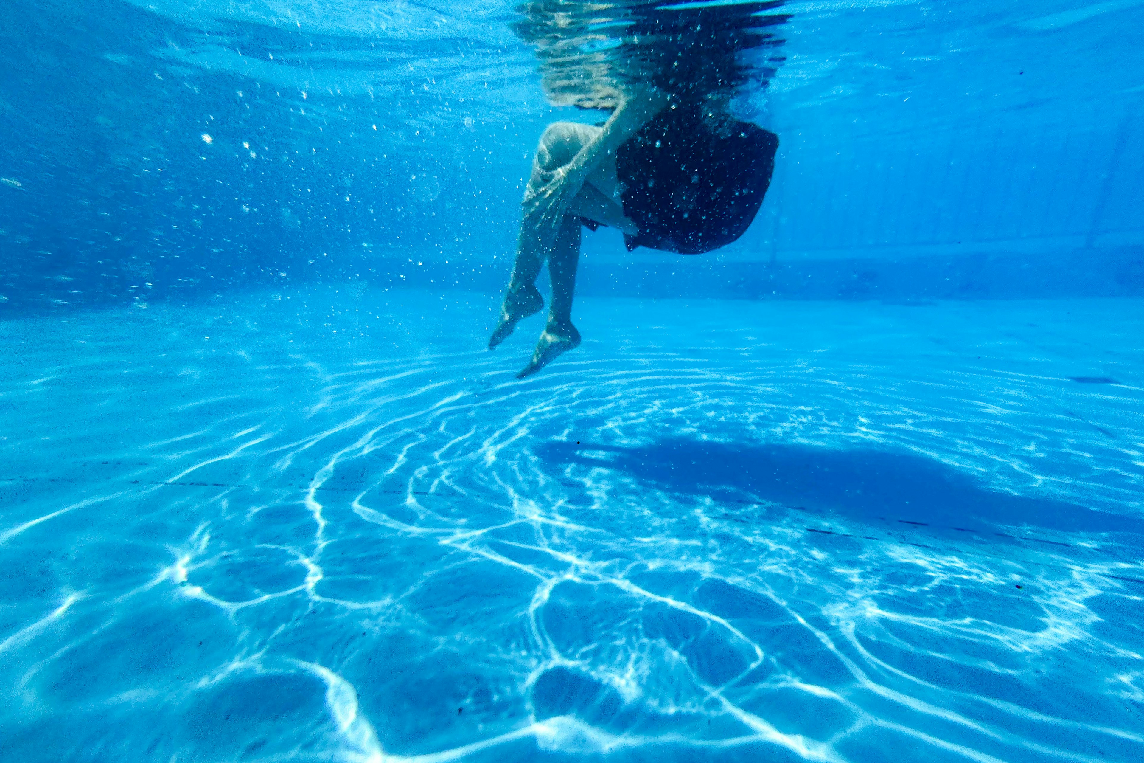 Bambino che gioca sott'acqua in acqua blu con riflessi di luce