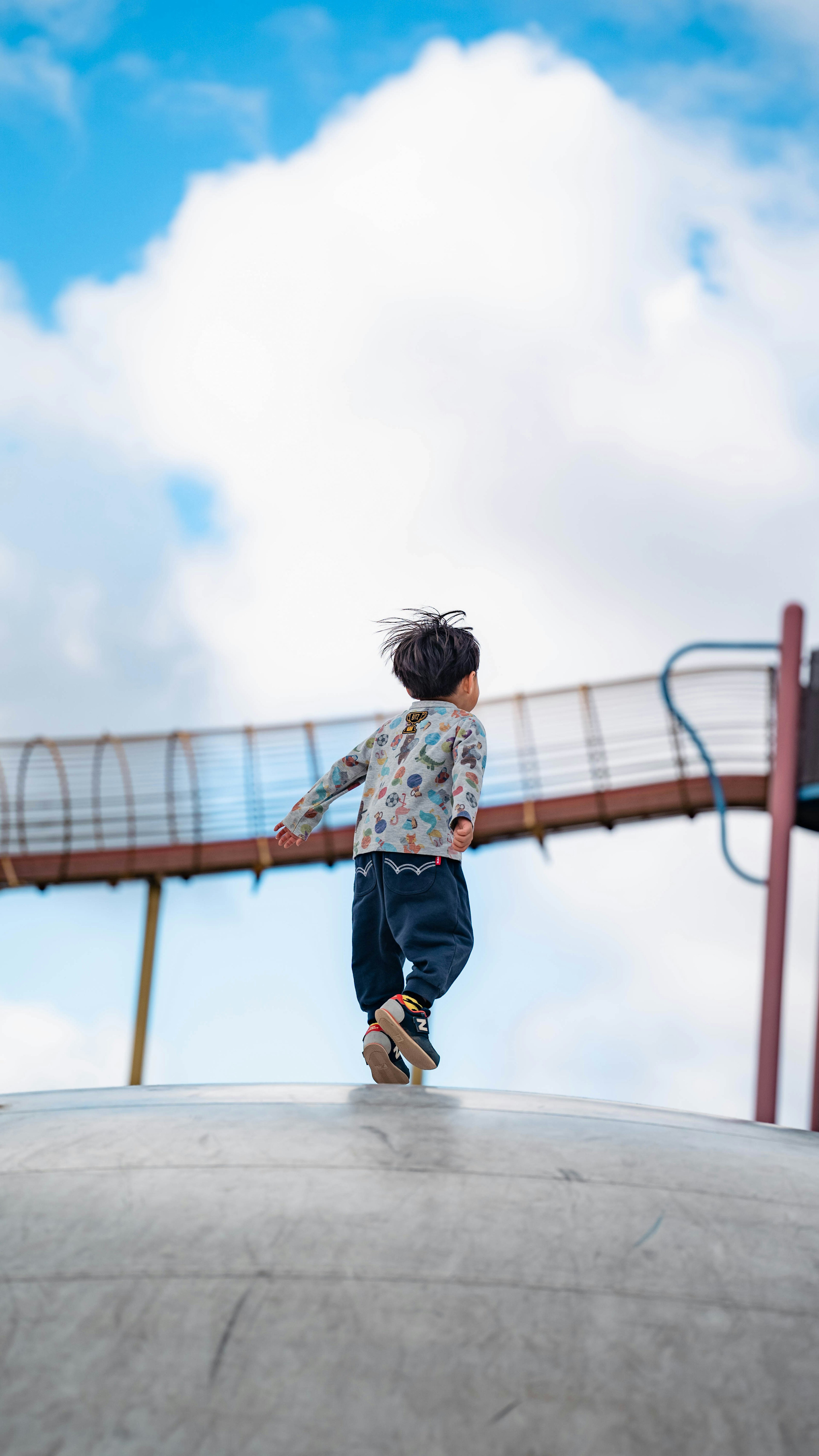 Un bambino che corre su una struttura da gioco con cielo blu e nuvole bianche sullo sfondo