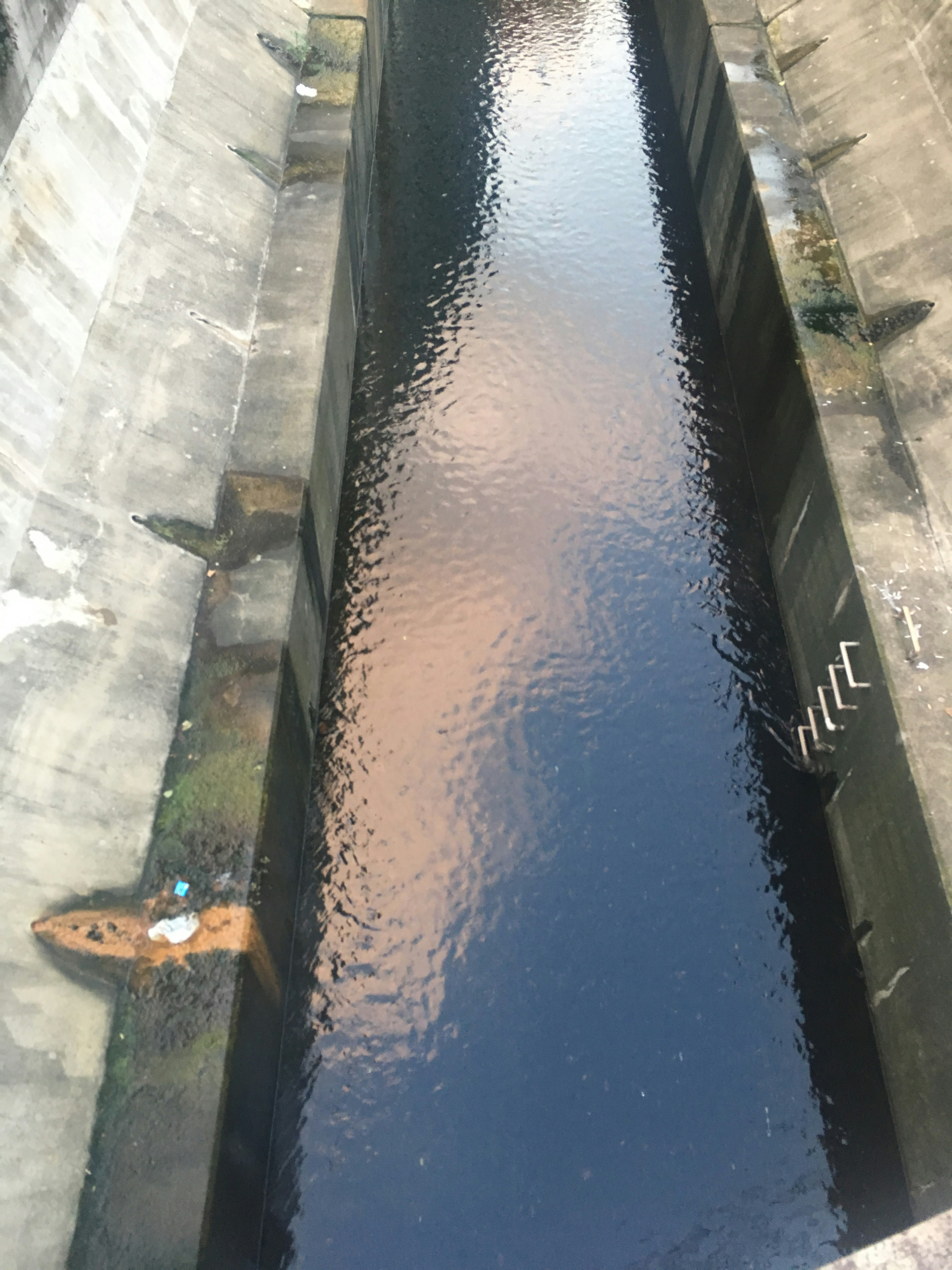 Calm water surface of a canal viewed from above with concrete walls