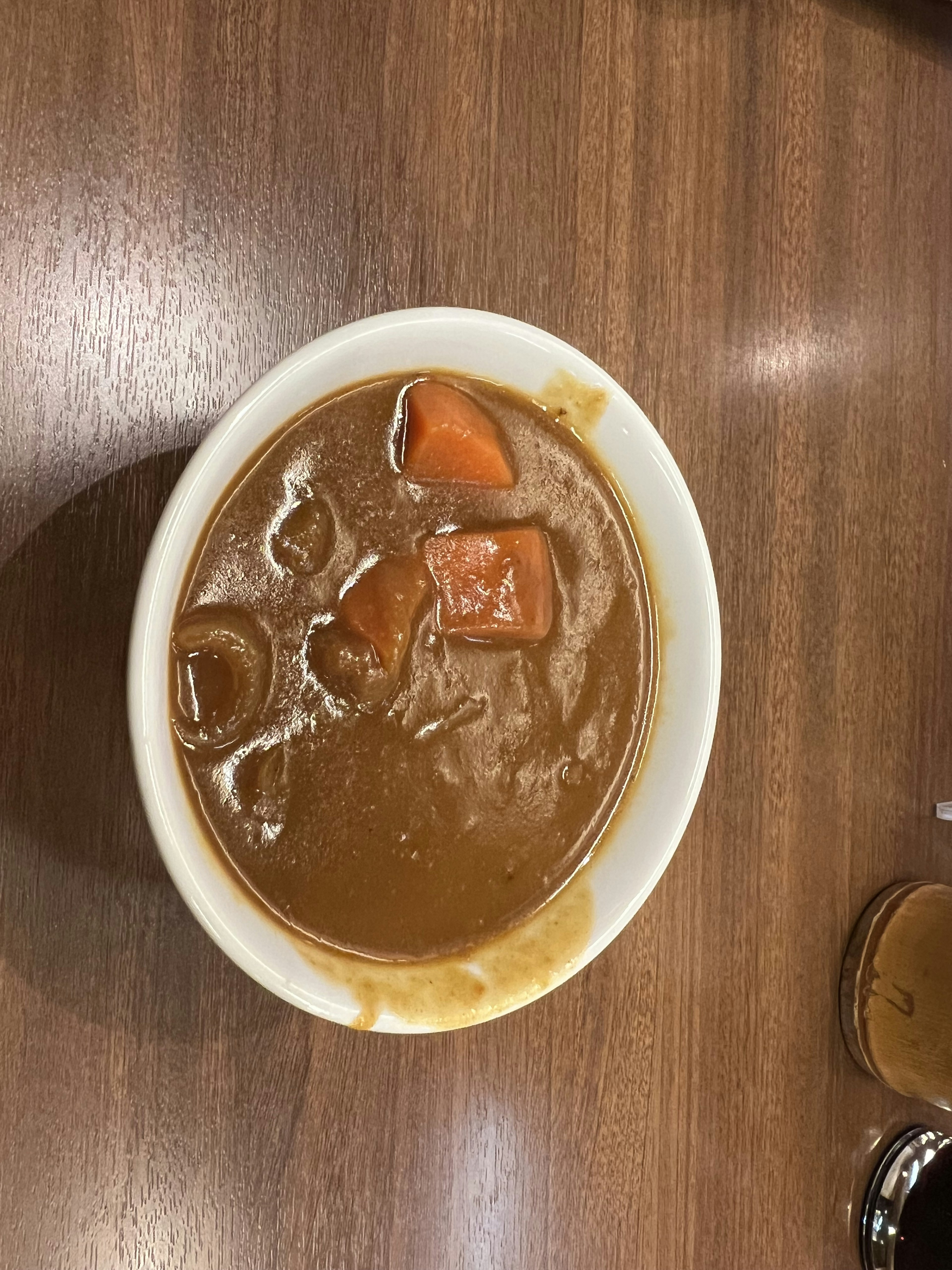 Bowl of brown curry with carrots on a wooden table