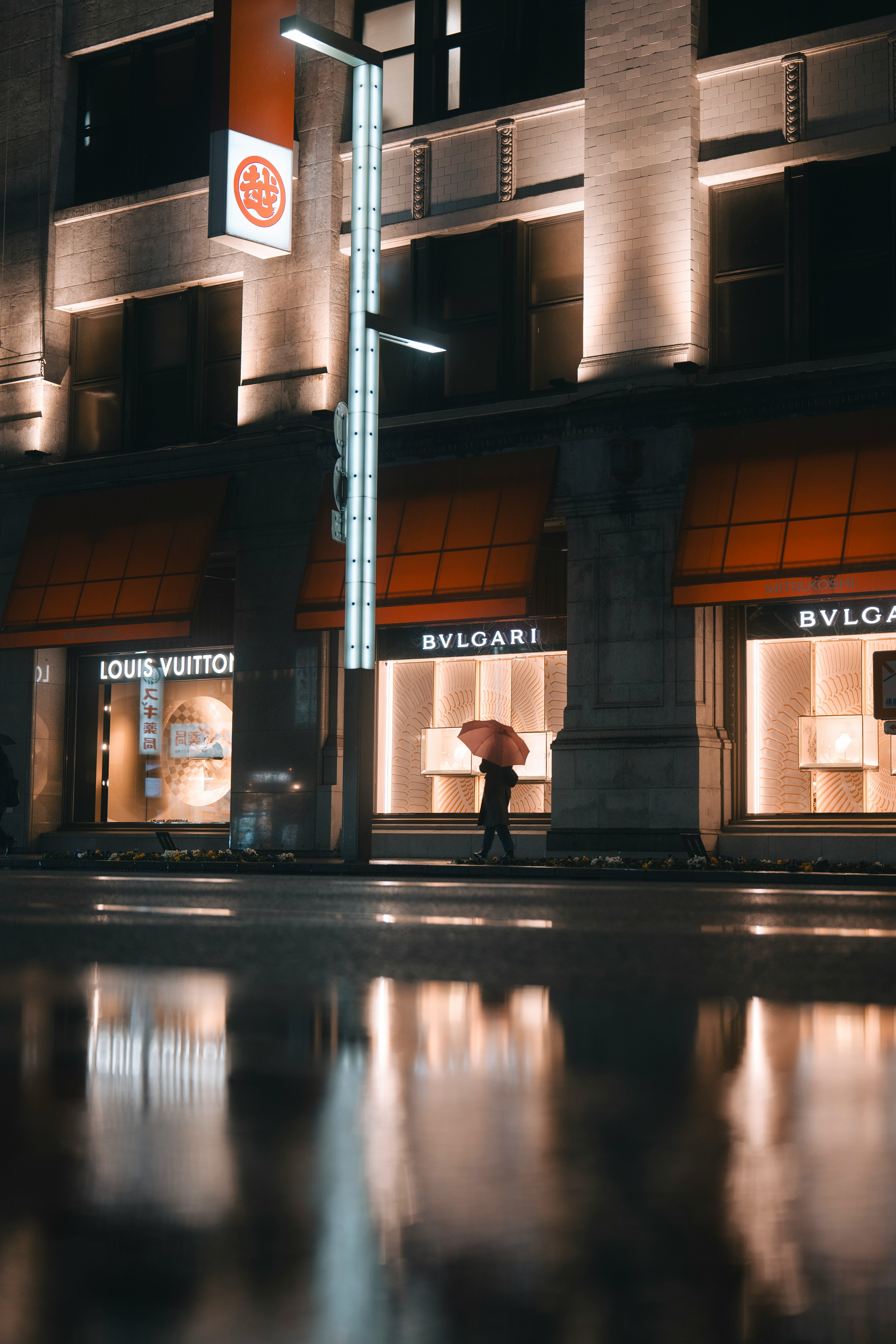 Luxury storefronts at night with reflections on a wet sidewalk