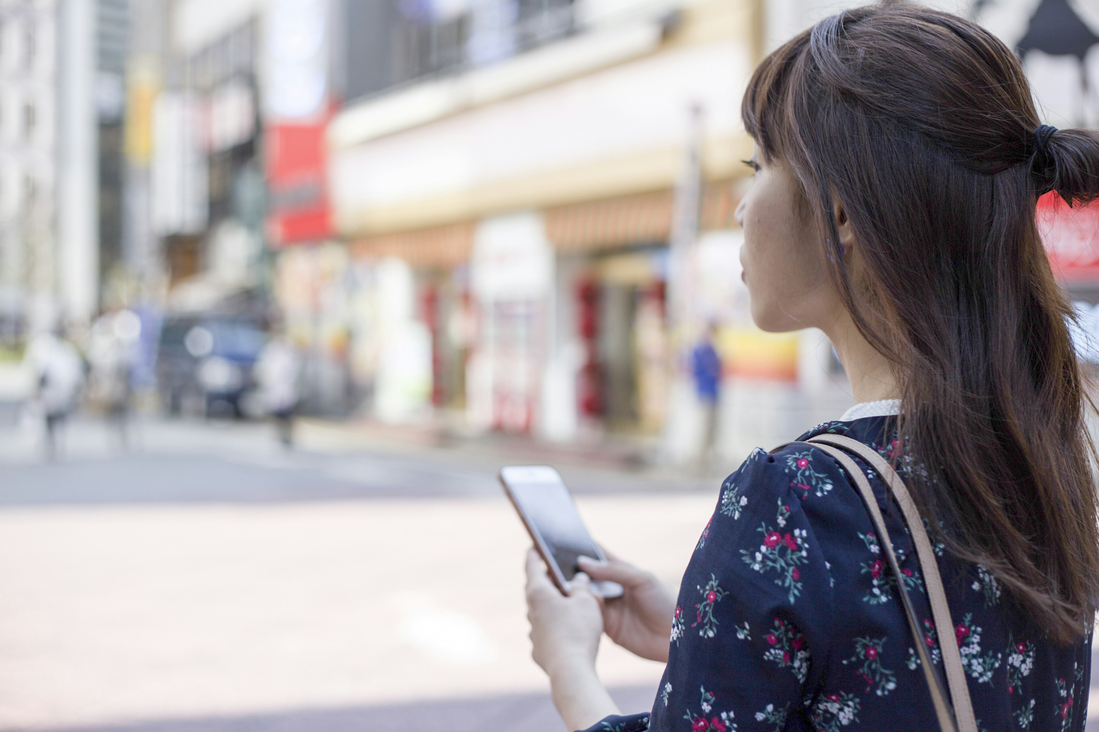 Una mujer sosteniendo un teléfono inteligente de pie en una esquina de la calle