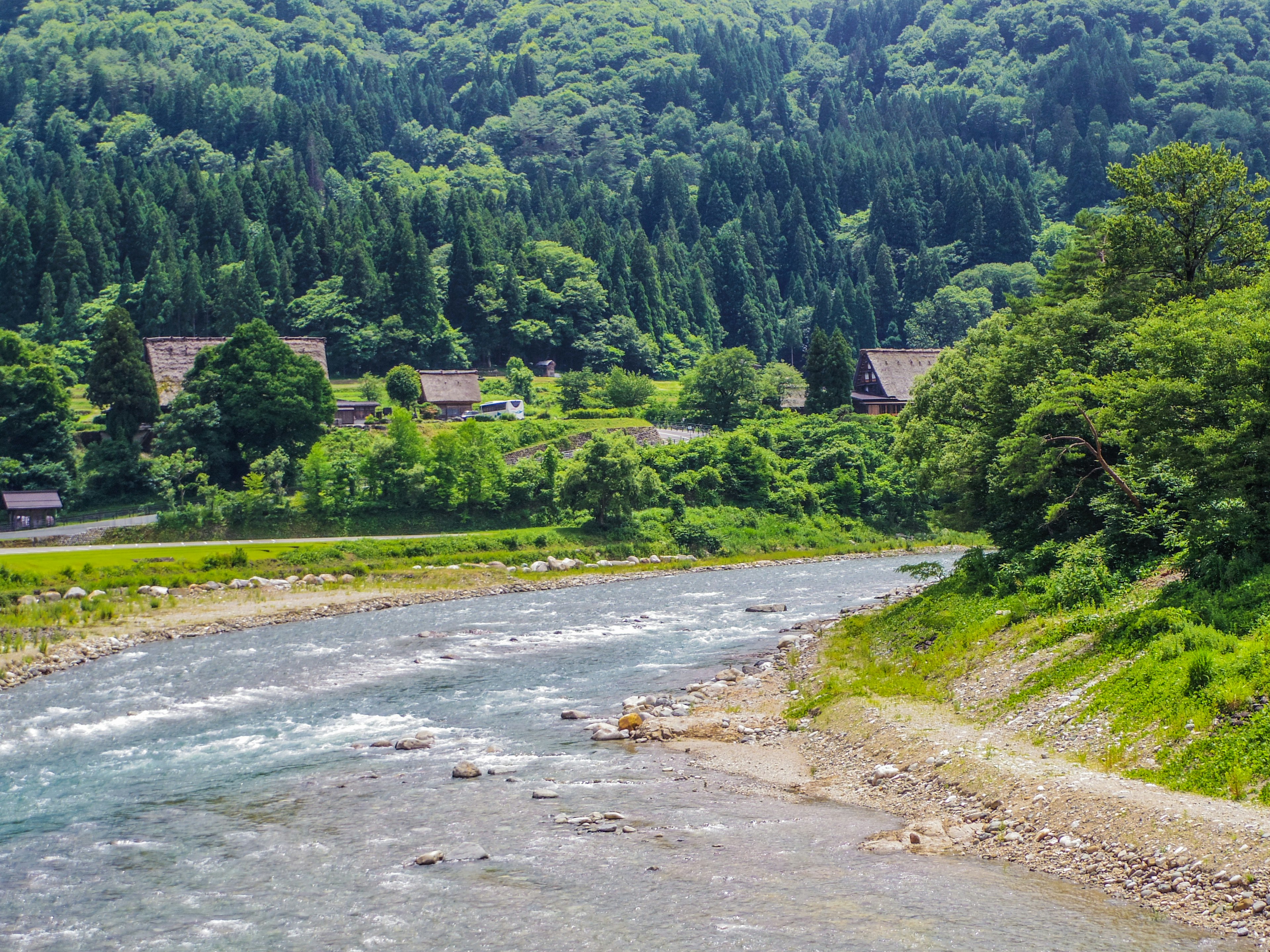 Montagne verdi lussureggianti con un fiume che scorre case tradizionali adagiate sulla collina