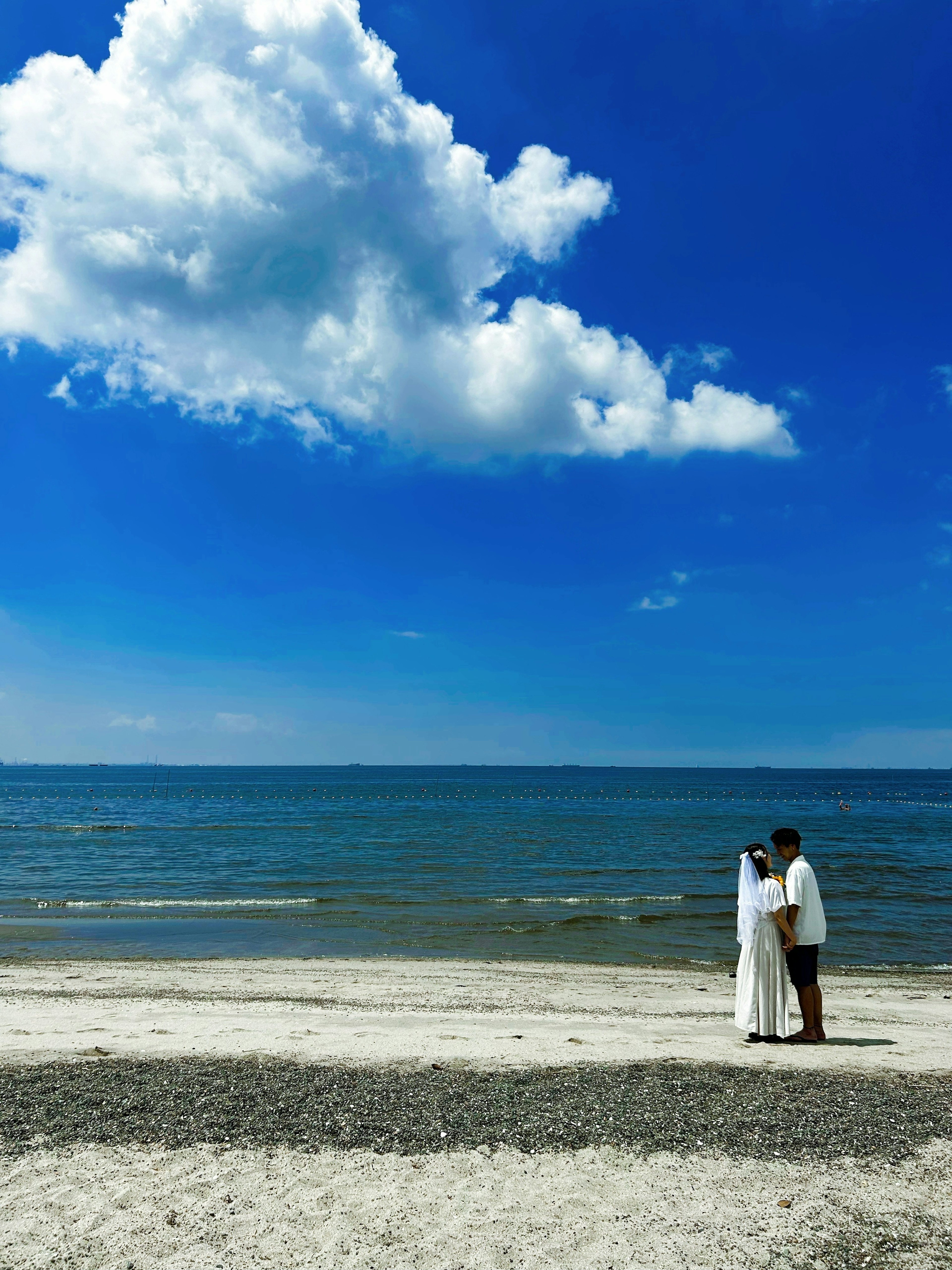 Pareja besándose en una playa bajo un cielo azul con nubes esponjosas