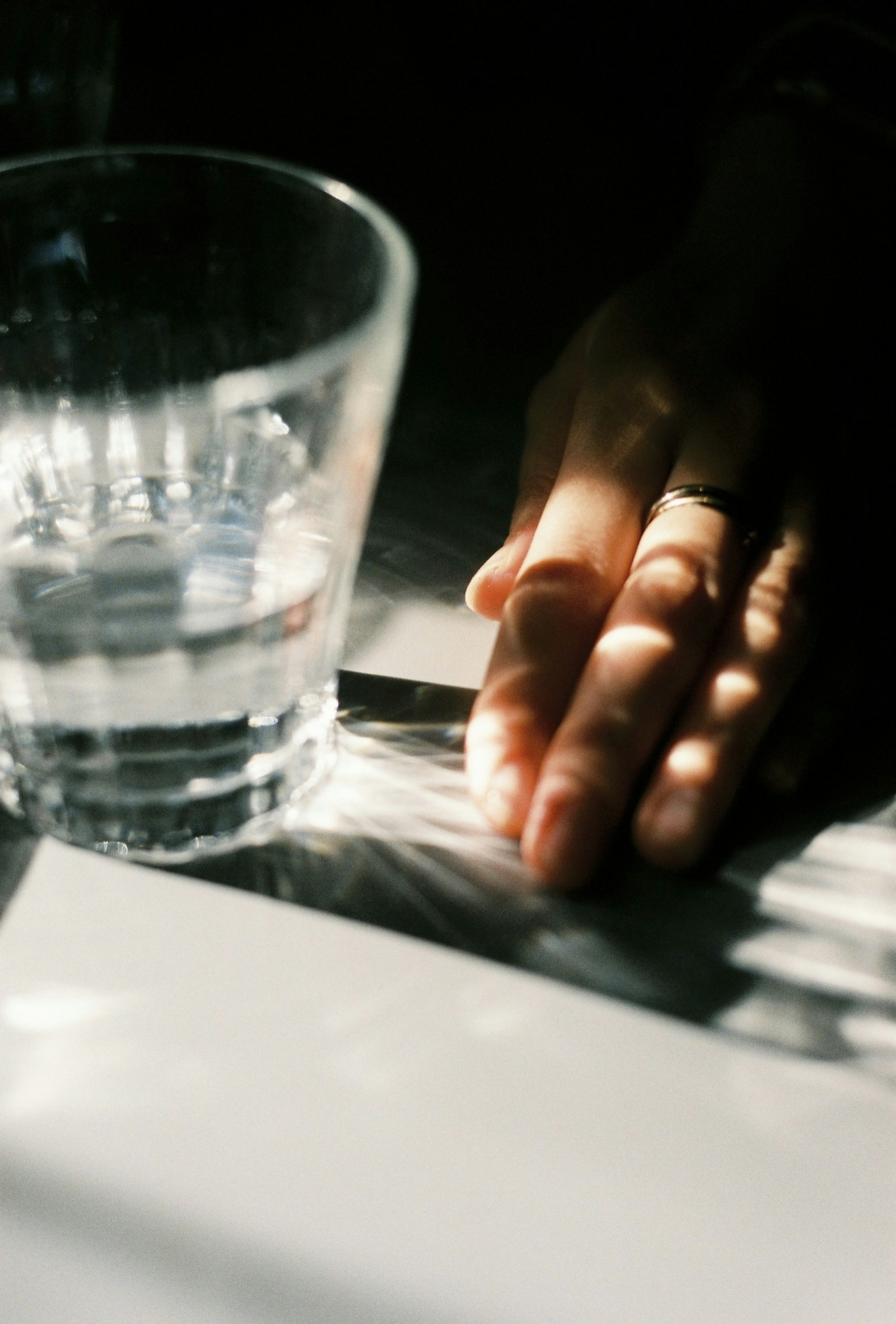 A hand resting beside a glass of water on a table with light reflections