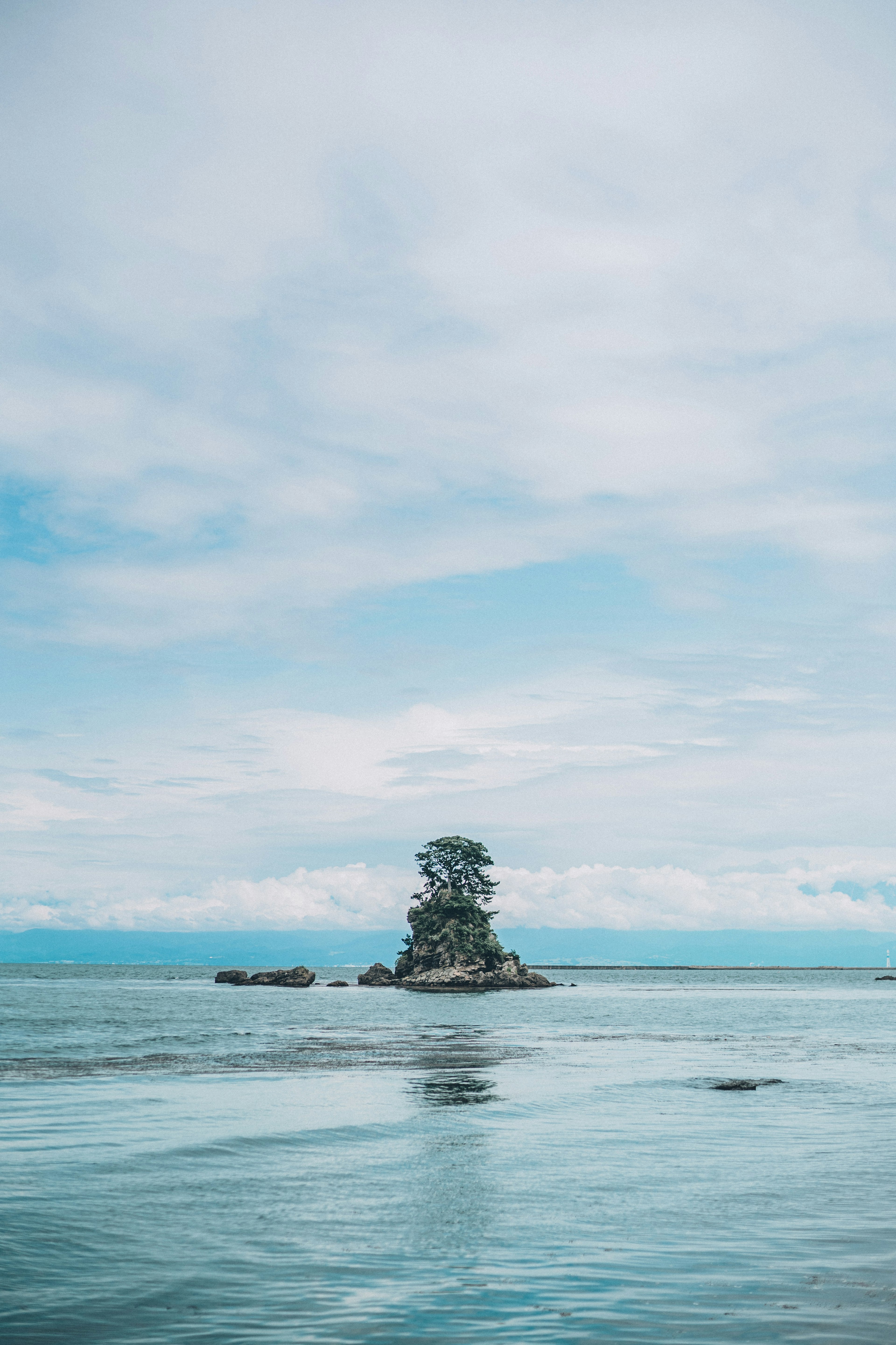 Eine kleine Insel mit Bäumen umgeben von ruhigem blauem Wasser und bewölktem Himmel