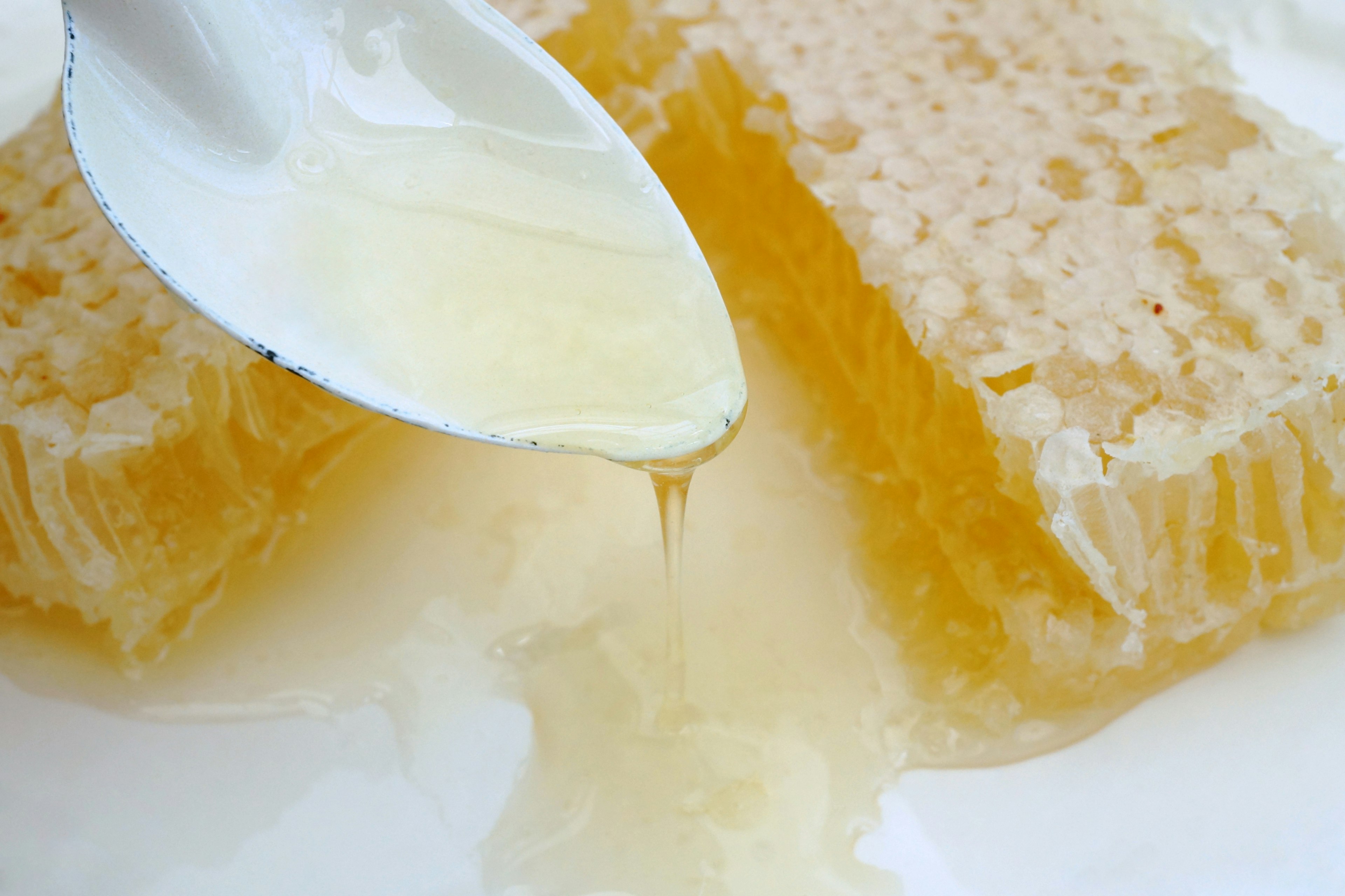 Miel doré s'écoulant de la ruche avec une cuillère blanche