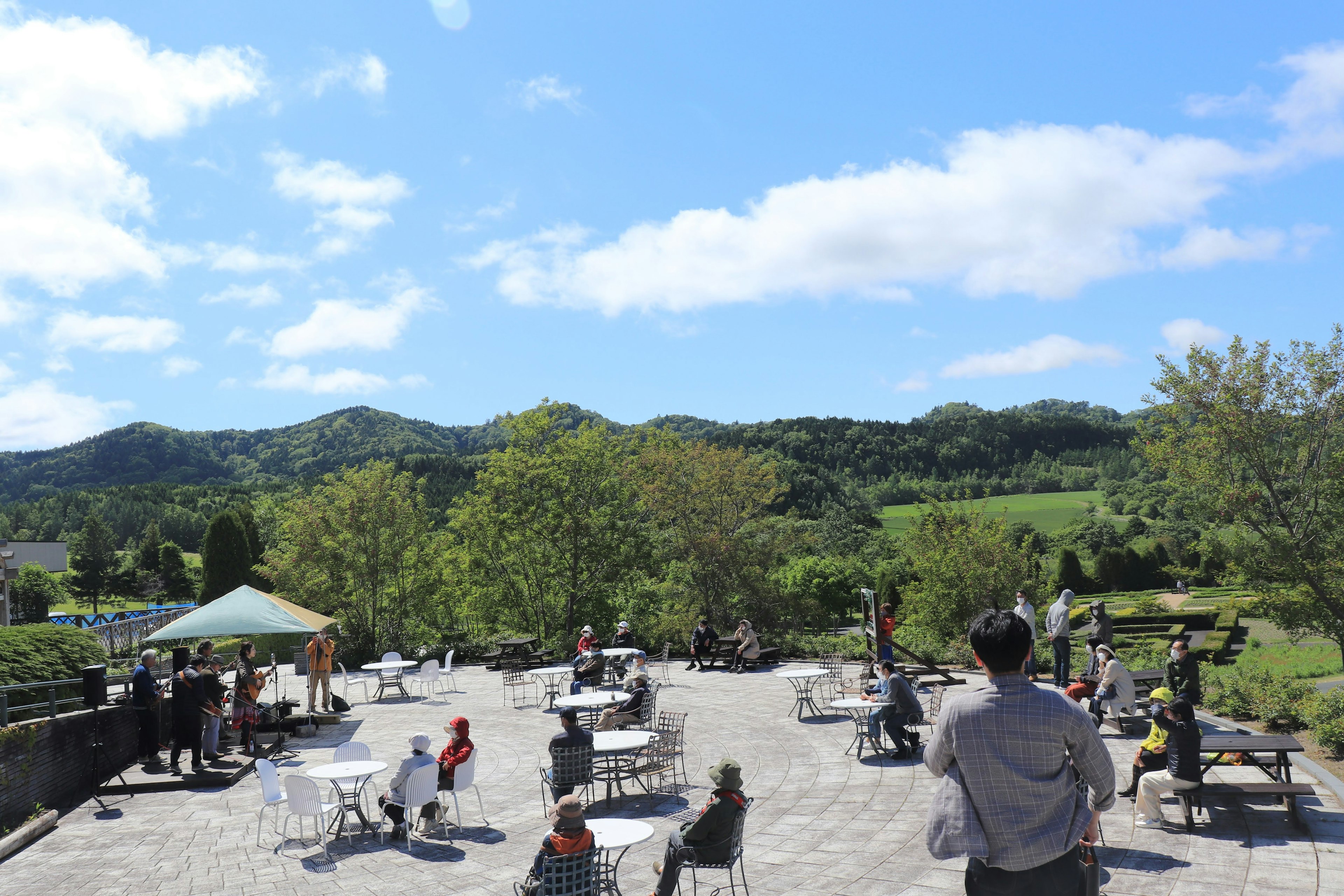 Outdoor cafe terrace with people enjoying under a blue sky lush green mountains in the background