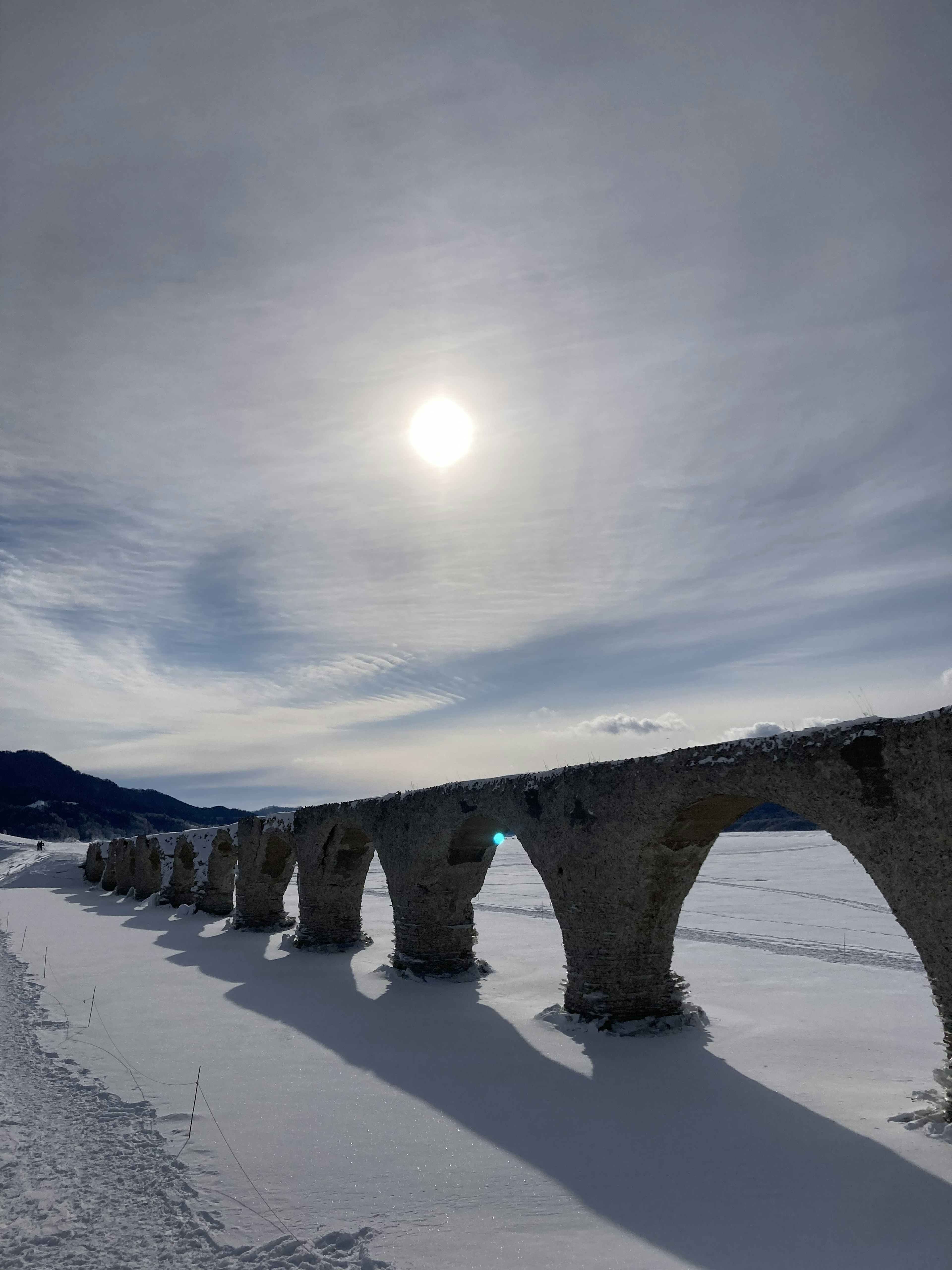 Un paisaje nevado con un antiguo puente de arco bajo el sol