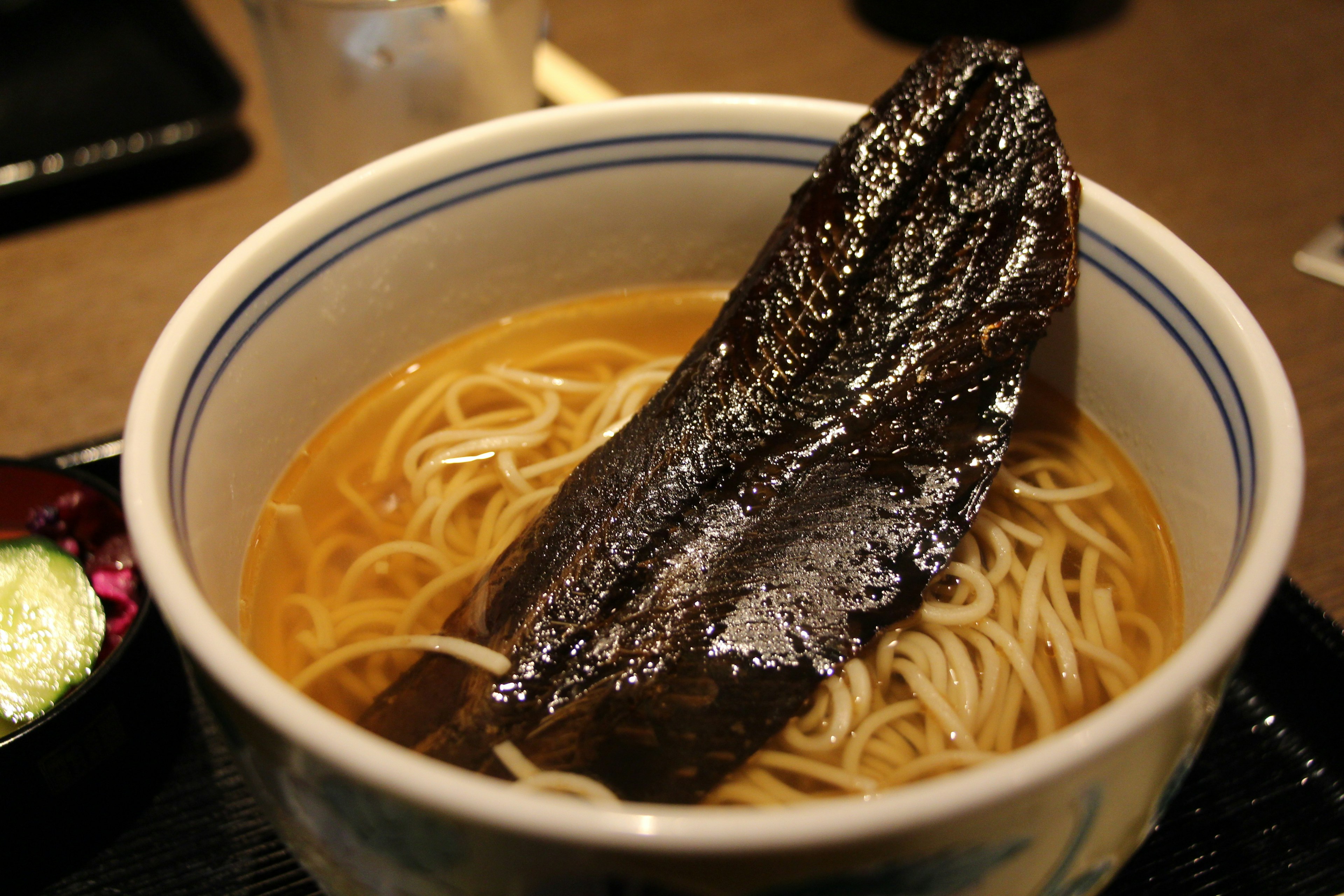 Bowl of noodle soup featuring thin noodles and a large dark ingredient