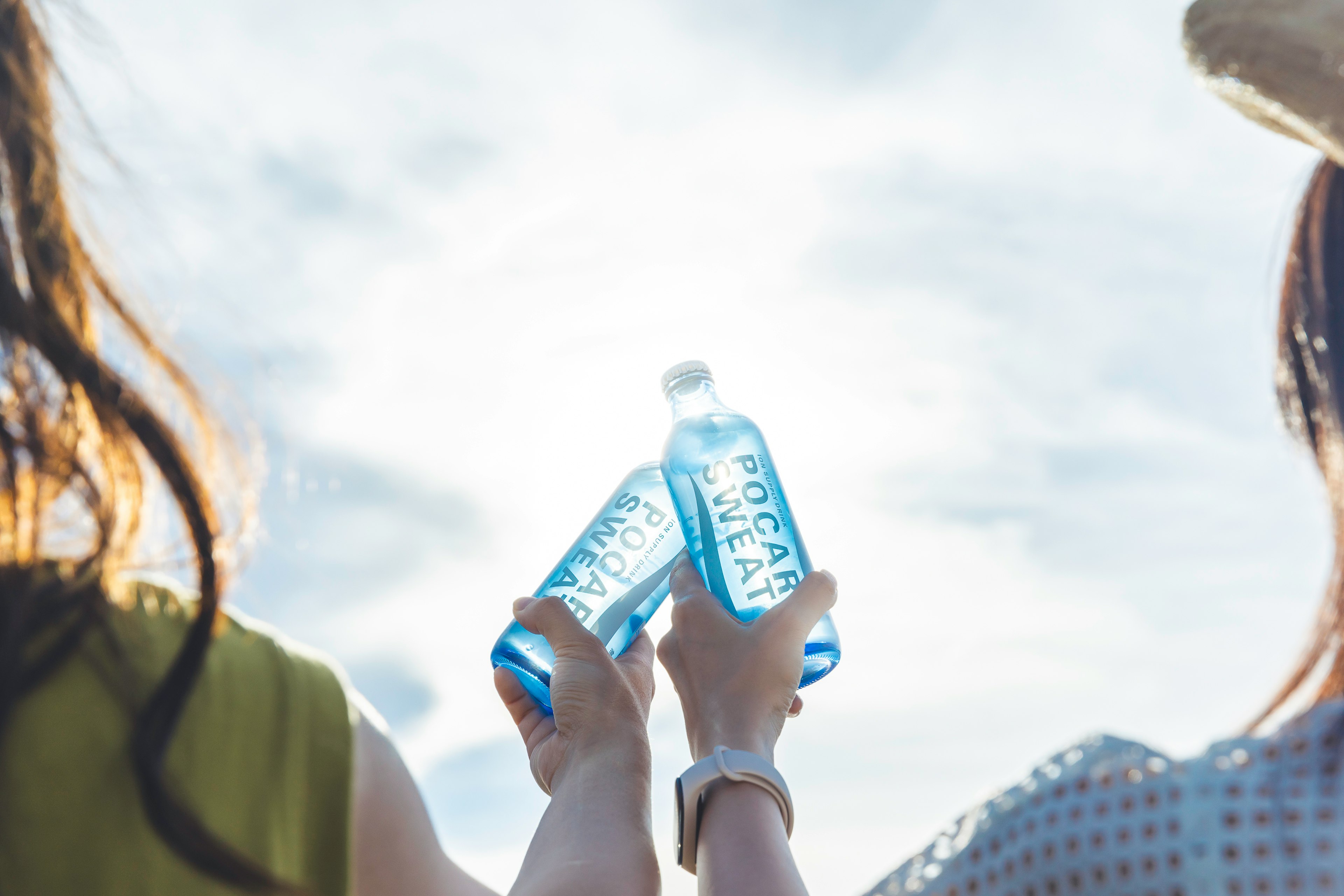 Two women holding blue water bottles up towards the sky