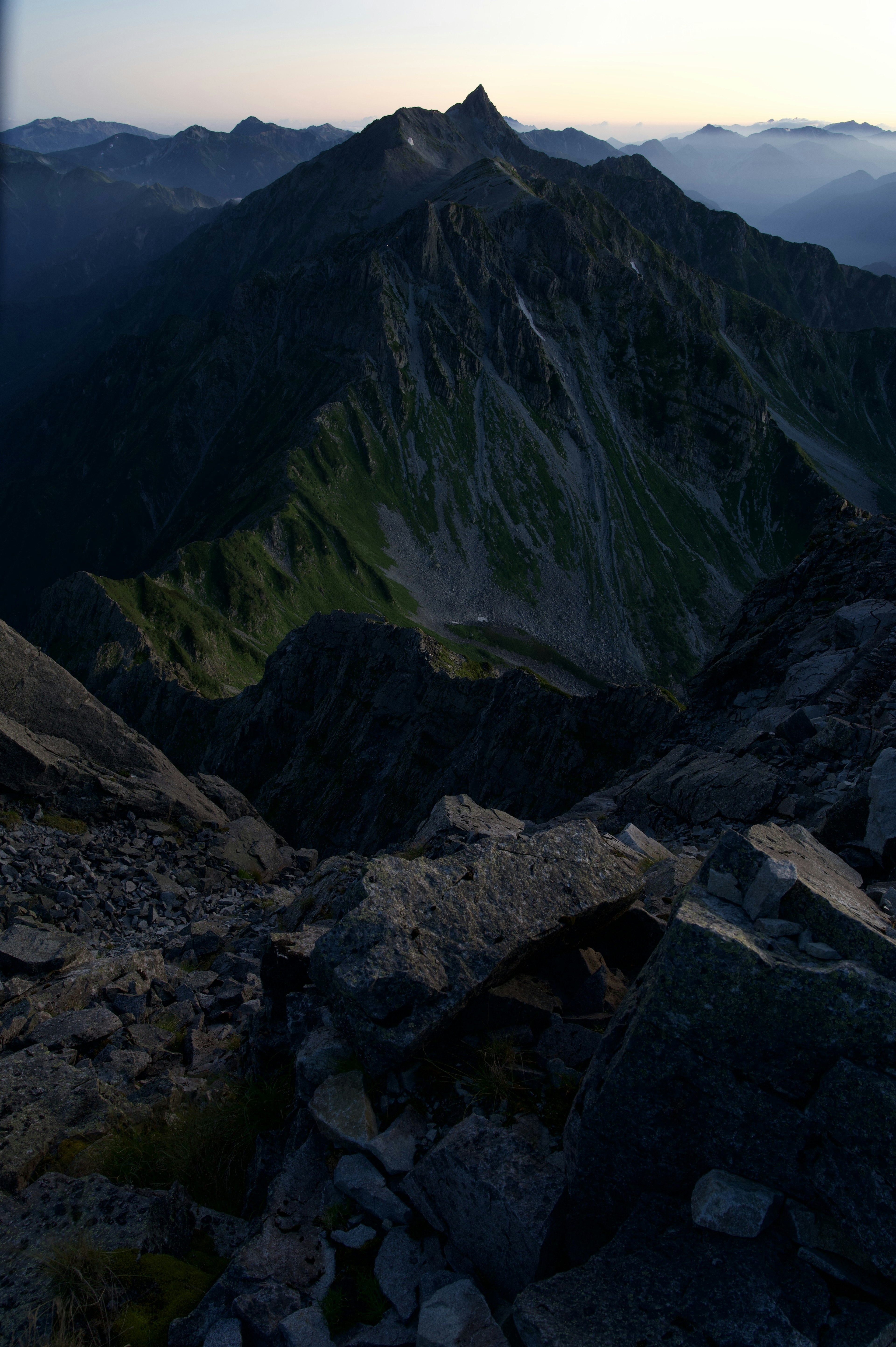 Paesaggio montano al crepuscolo, cime illuminate, pendii verdi, terreno accidentato