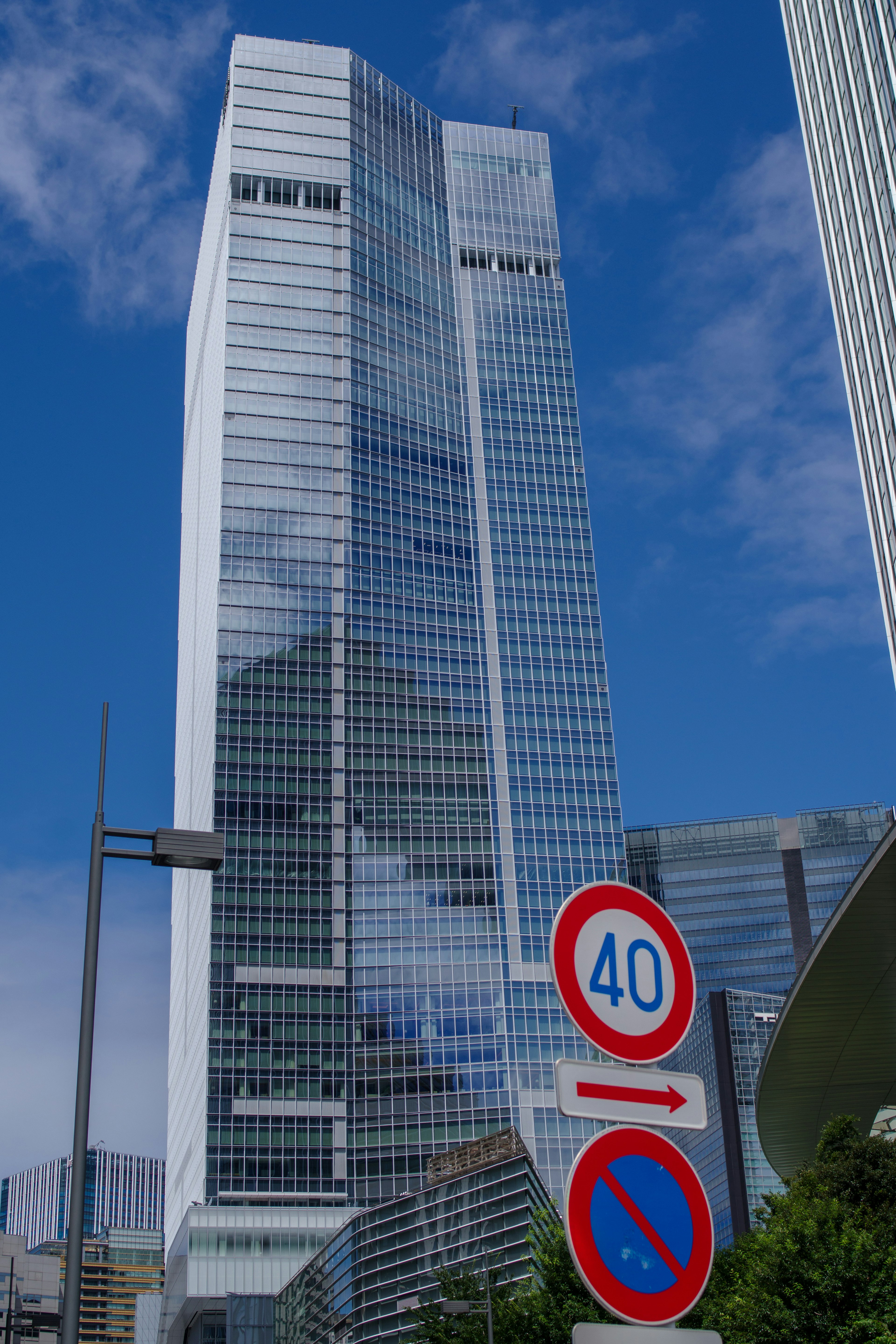 Photo of a skyscraper near traffic signs Glass building towering under blue sky