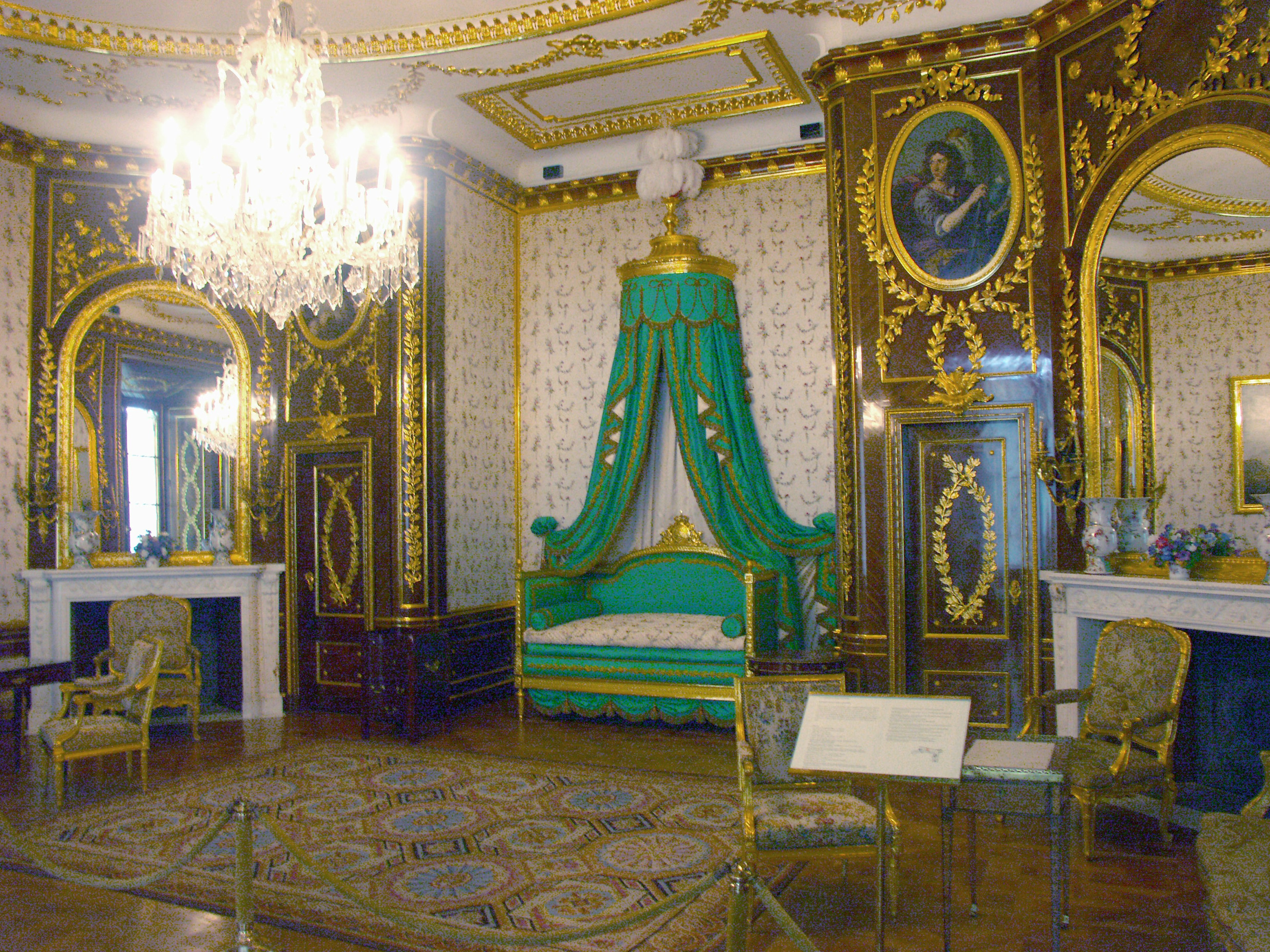 Lavishly decorated room featuring gold details a beautiful chandelier and a green-draped bed