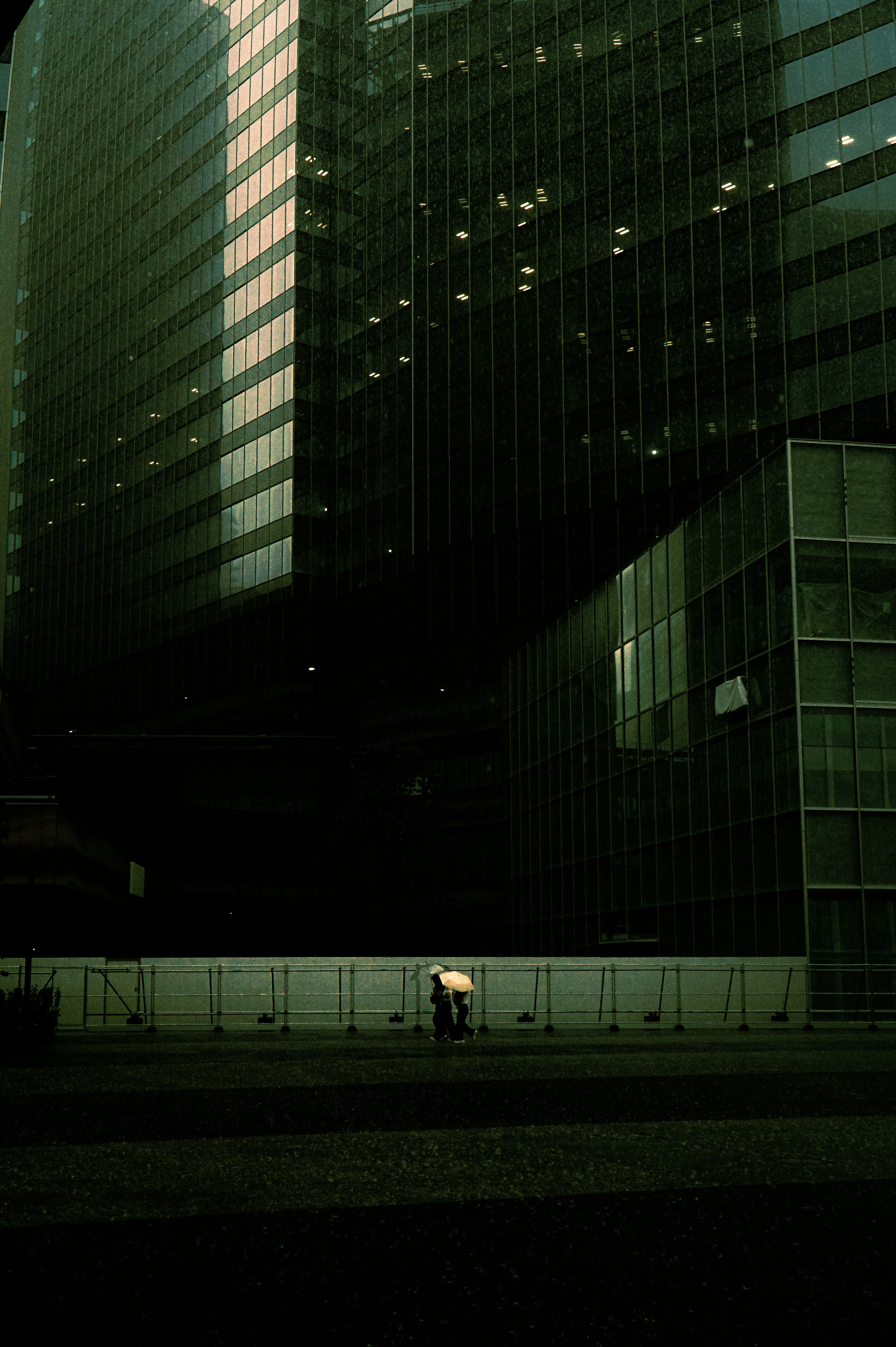 A person with an umbrella walking in the shadow of skyscrapers