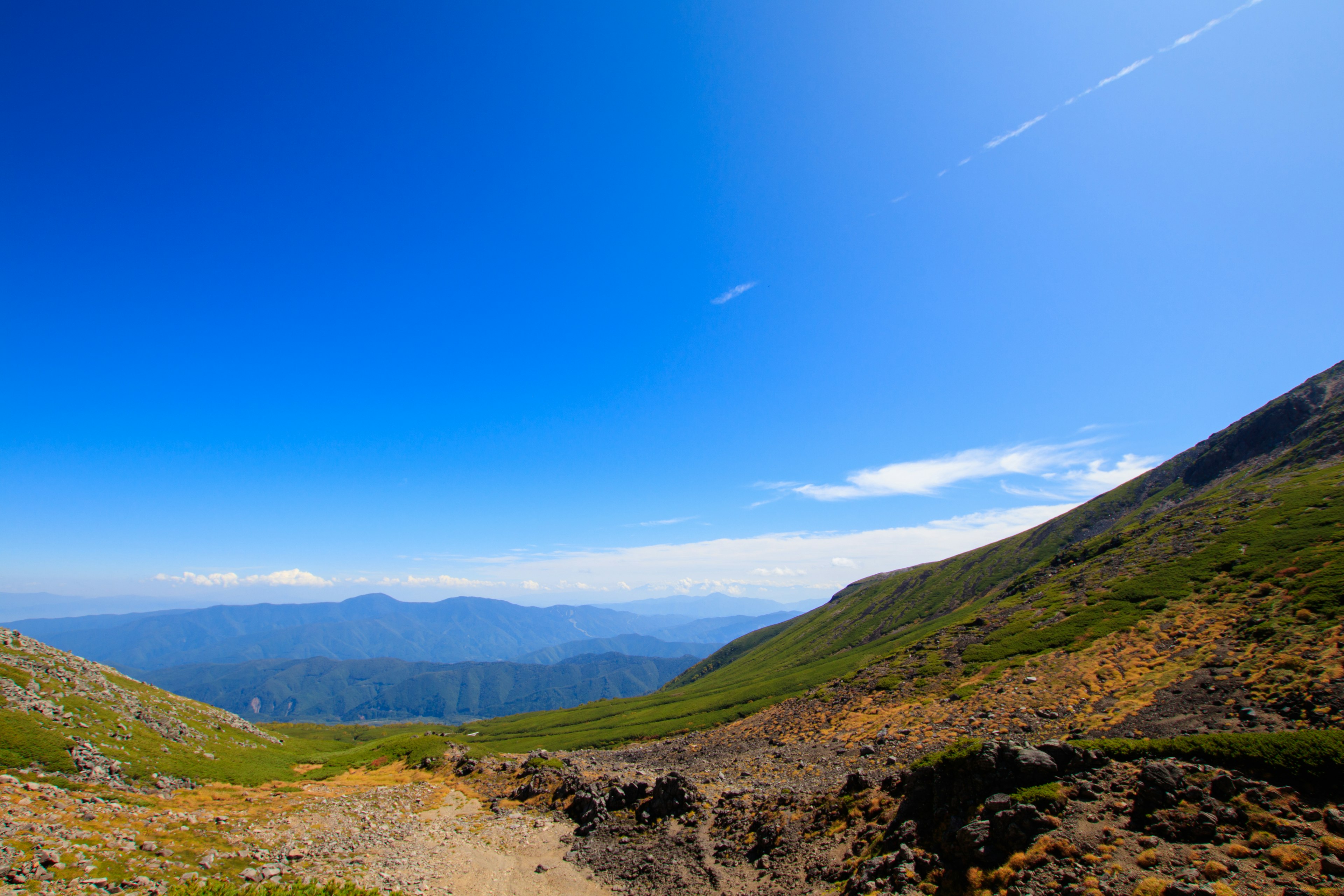 Vista panoramica di montagne e cielo blu con erba verde e sentiero roccioso